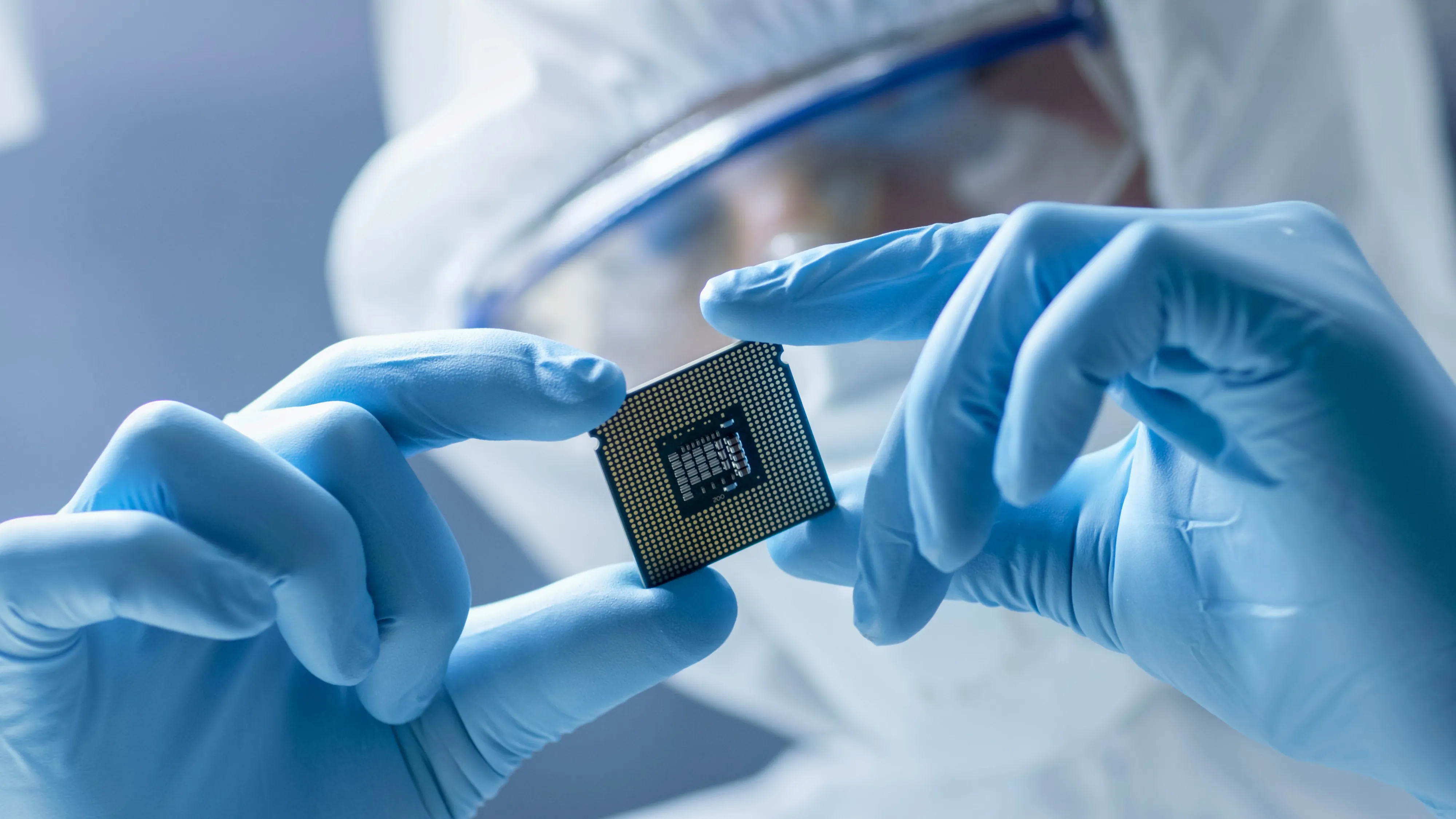 In ultra modern electronic manufacturing factory, design engineer in sterile coverall holds microchip with gloves and examines it