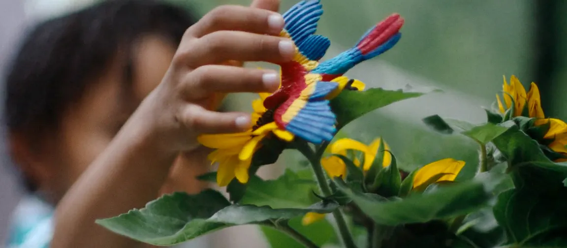 Hand of a little girl placing a gum bird on a flower