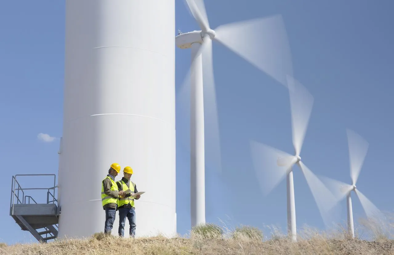 Two professionals are standing in front of wind turbines.