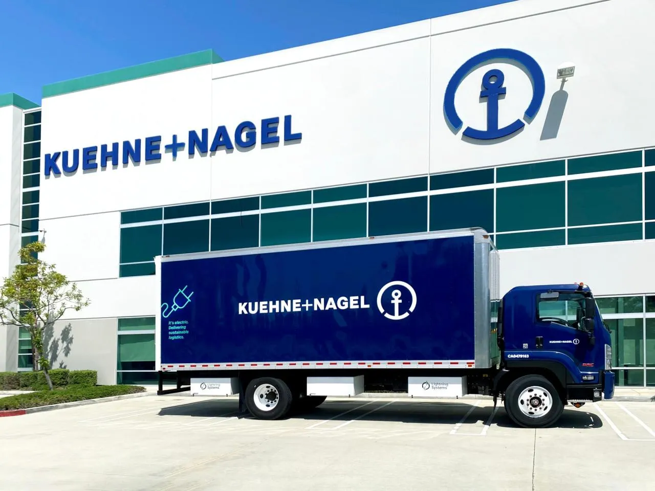 Electric Kuehne+Nagel truck in front of a Kuehne+Nagel warehouse at a sunny day.
