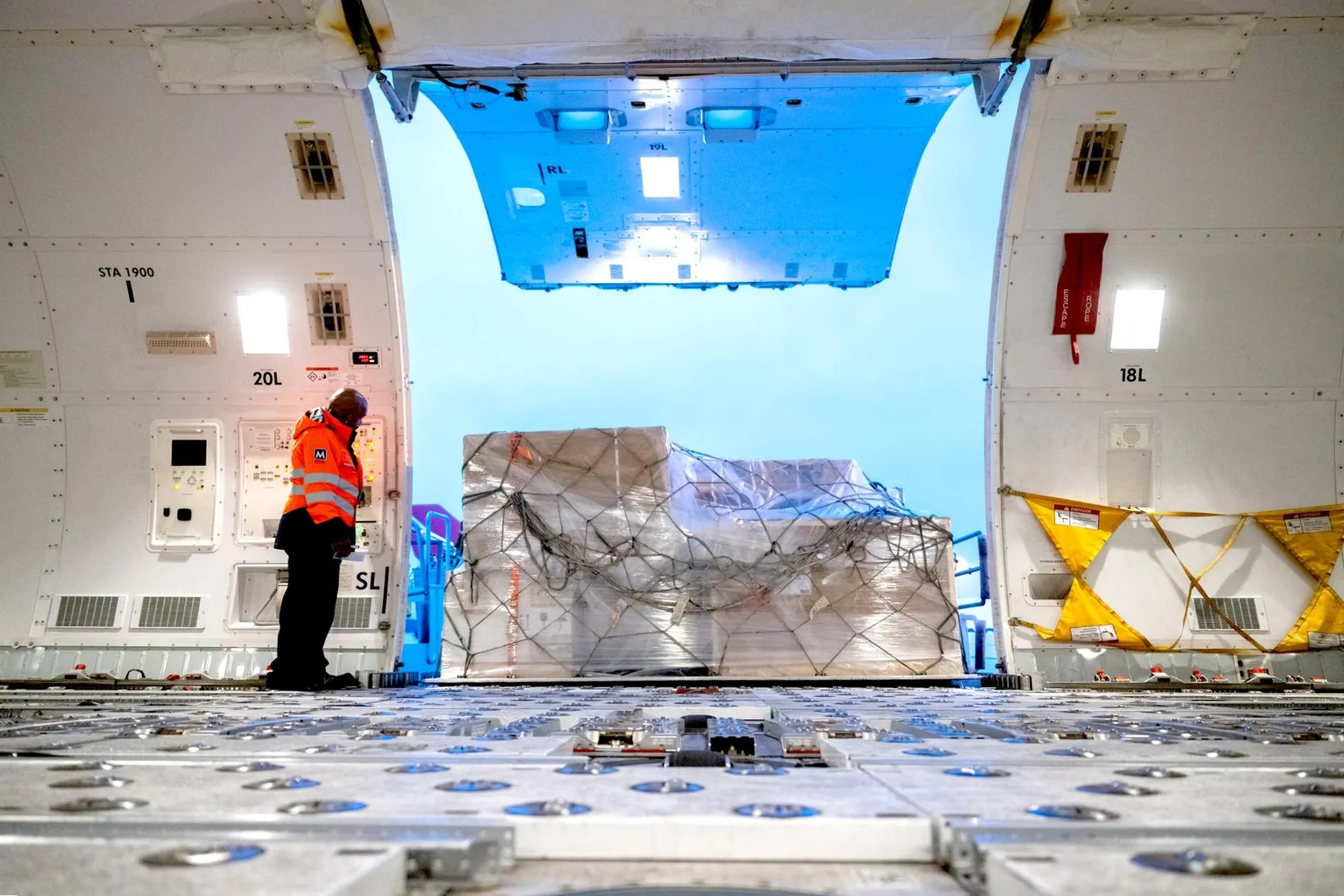 Air cargo being loaded into a freighter aircraft, with secured freight pallets and a ramp worker operating loading equipment.