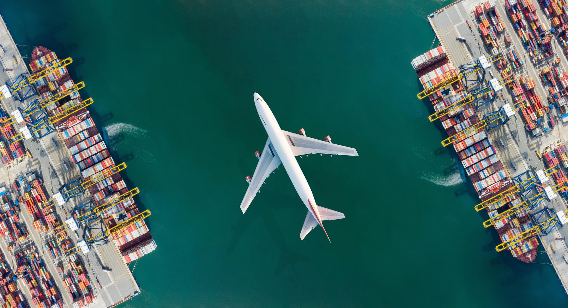 A plane flying over a harbour with container ships loading and unloading.