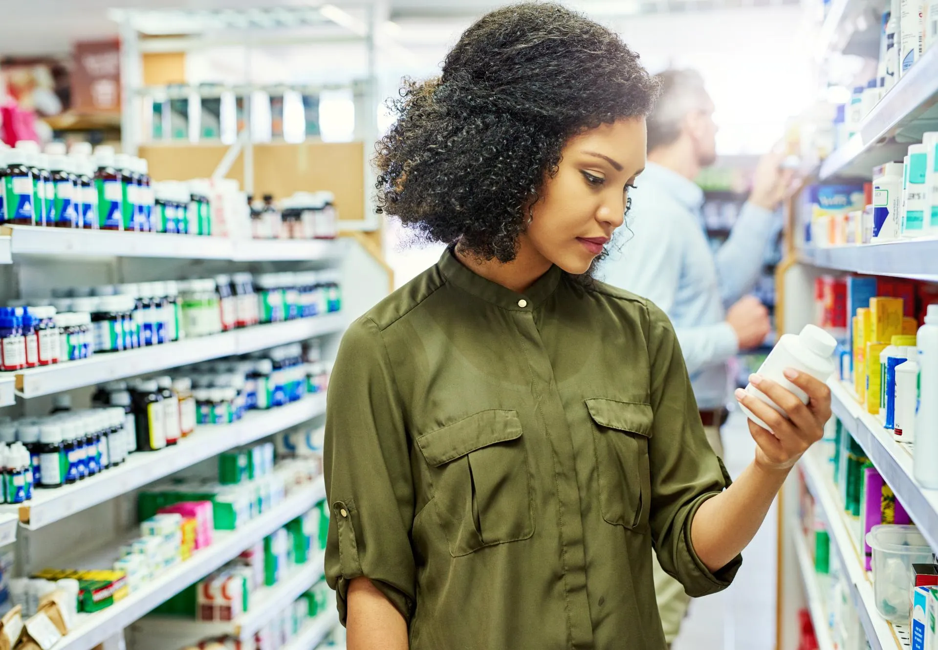 Woman reading a supplement bottle label while shopping in a pharmacy health aisle.