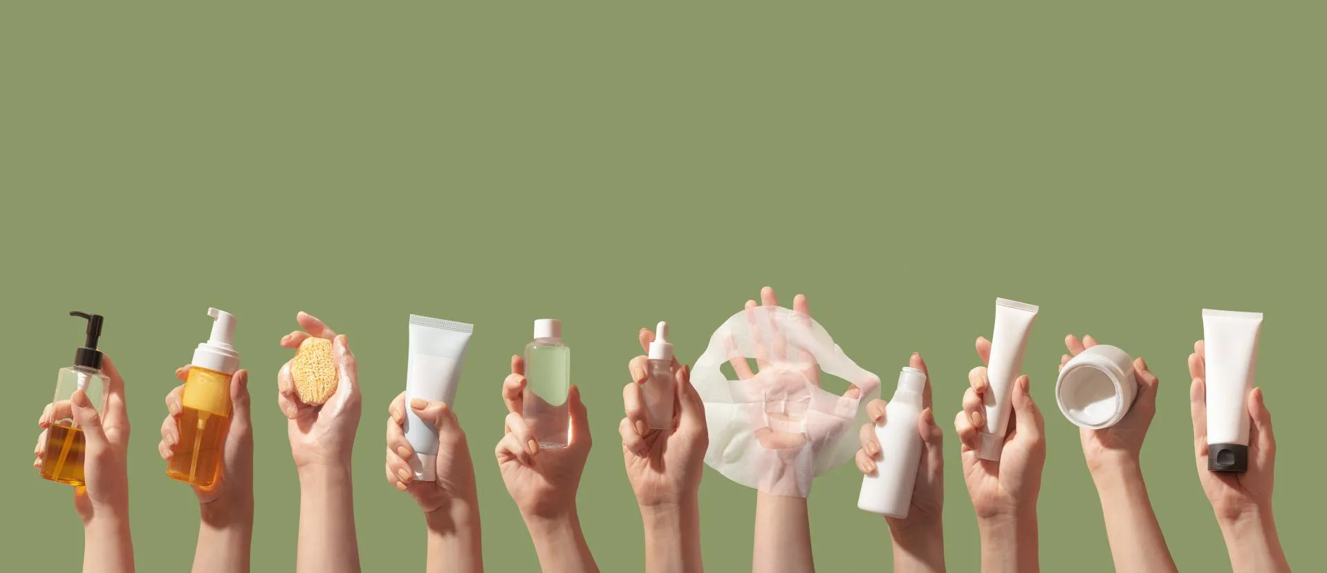 Hands holding bottles of different skincare and cosmetic products against a green background.