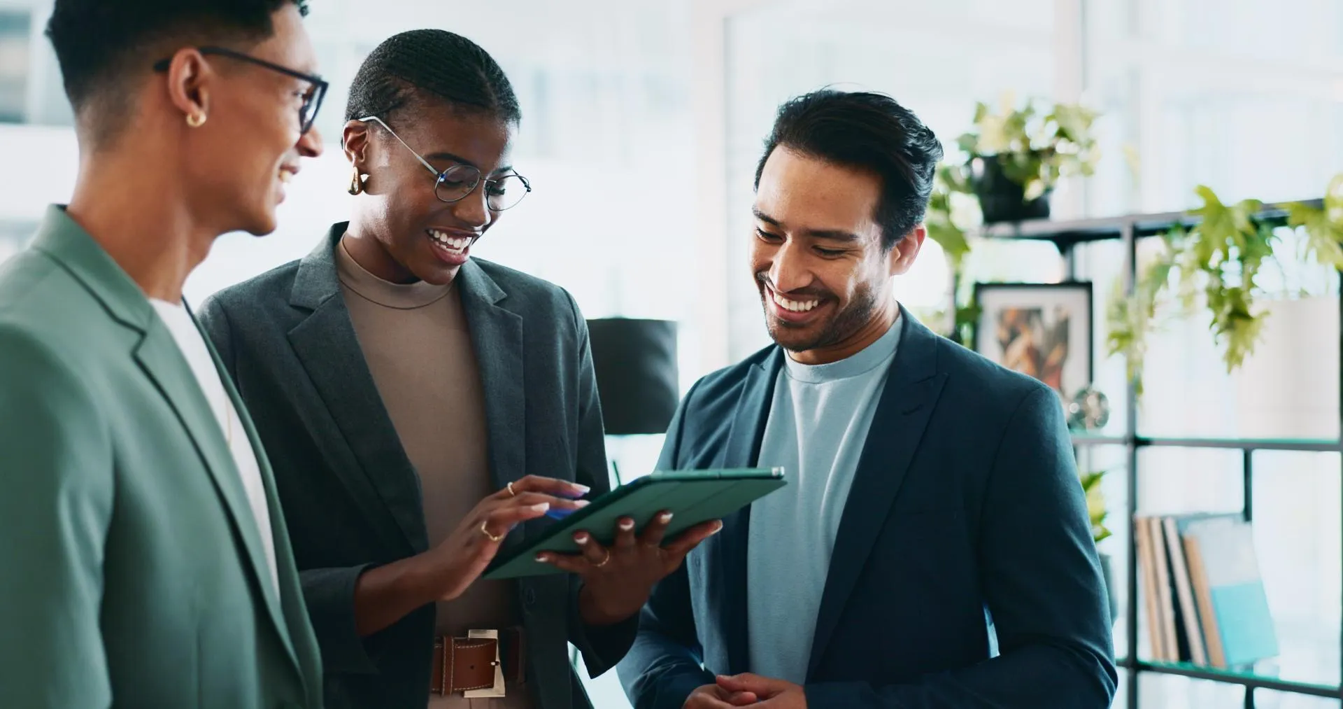 2 men and a woman colleagues laughing, looking at a tablet