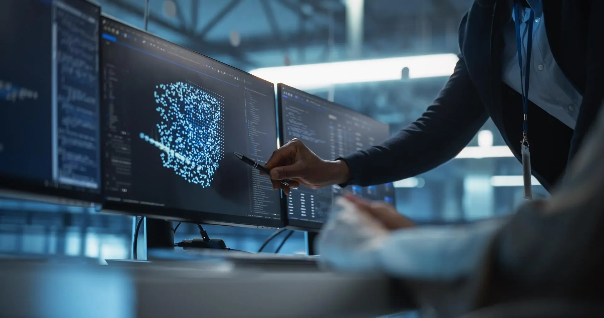 Person pointing at multiple computer screens displaying data and digital graphics in a modern workspace
