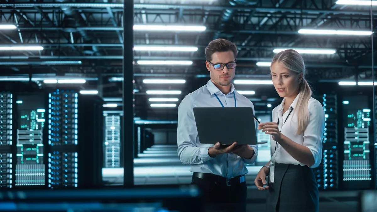 Two coworkers are checking data on the laptop in front of the server room.
