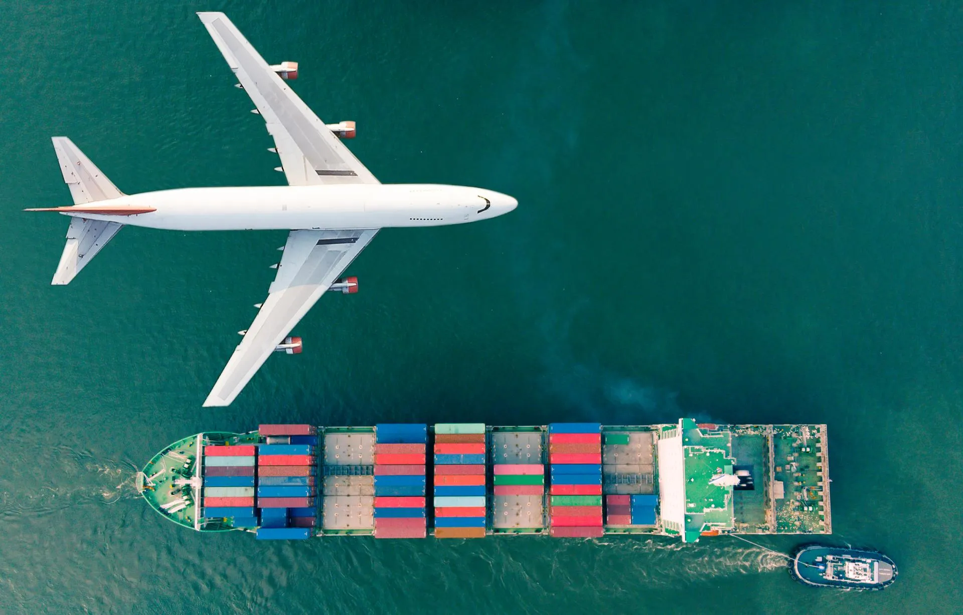 A plane and a vessel are shown from above with the plane flying above the ocean.