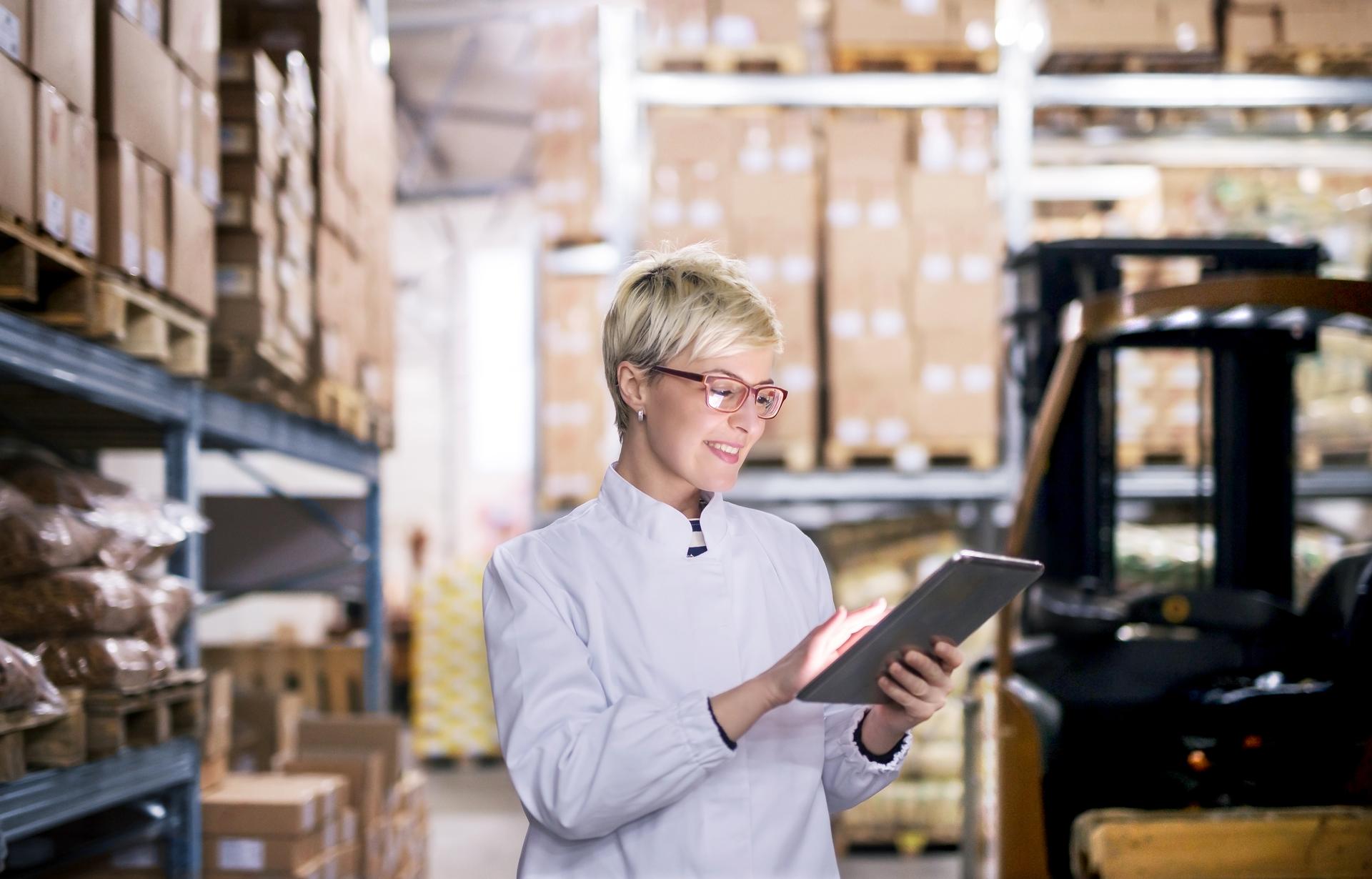 A warehouse worker who is smiling is interacting with a tablet.