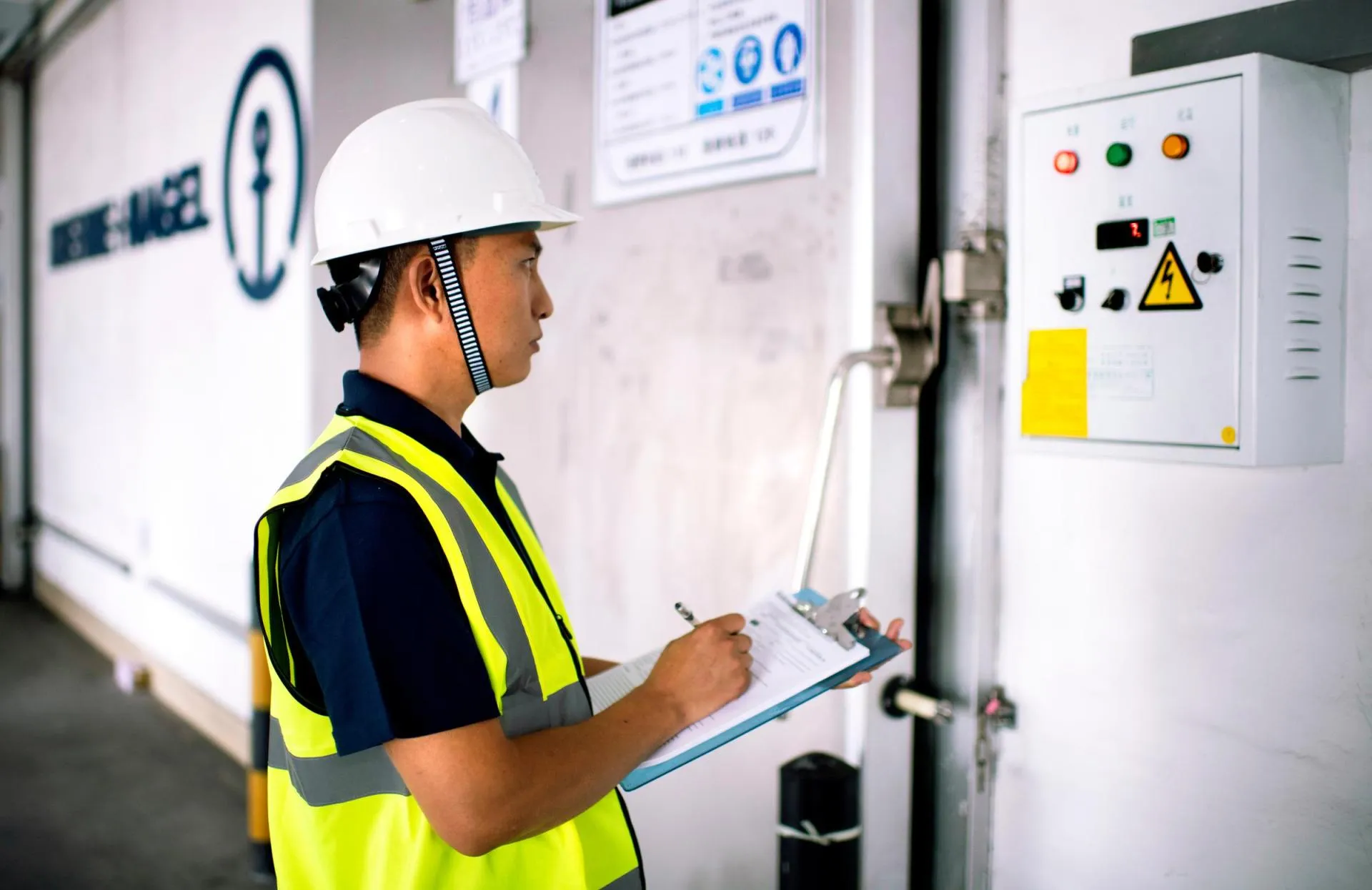 Industrial worker conducting safety inspection of electrical control equipment in a logistics facility.