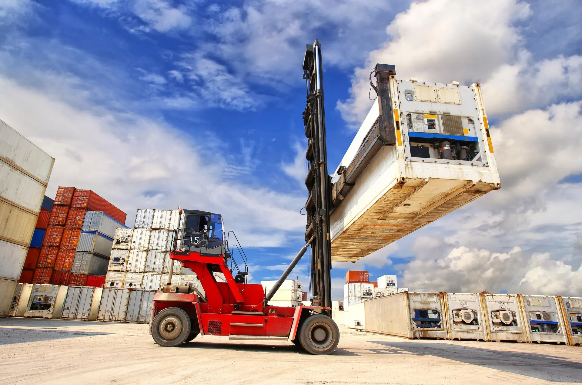 A large forklift is stacking a reefer container in the container yard.