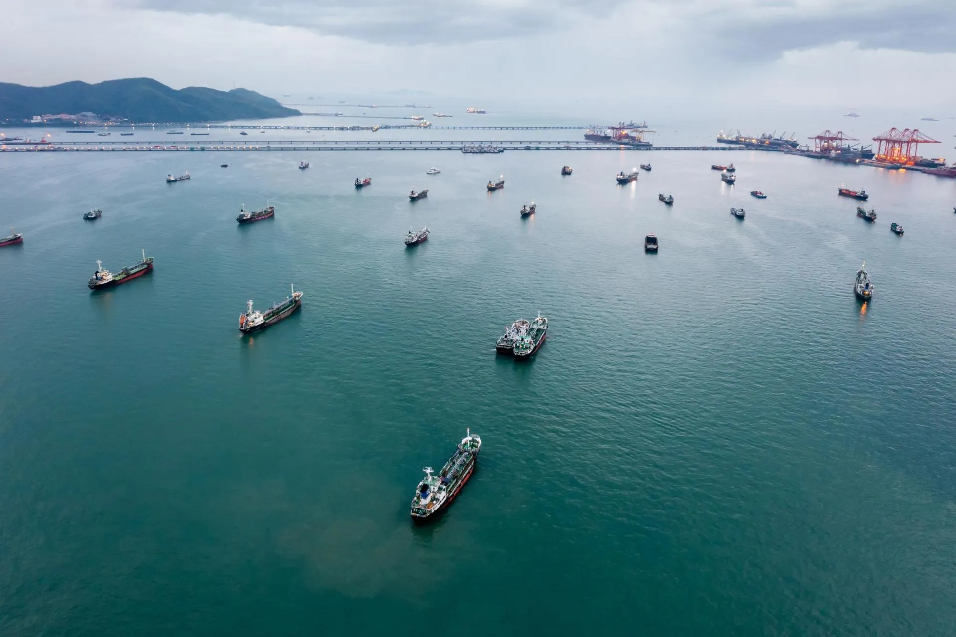 A group of transport ships waiting near a harbour at sea.