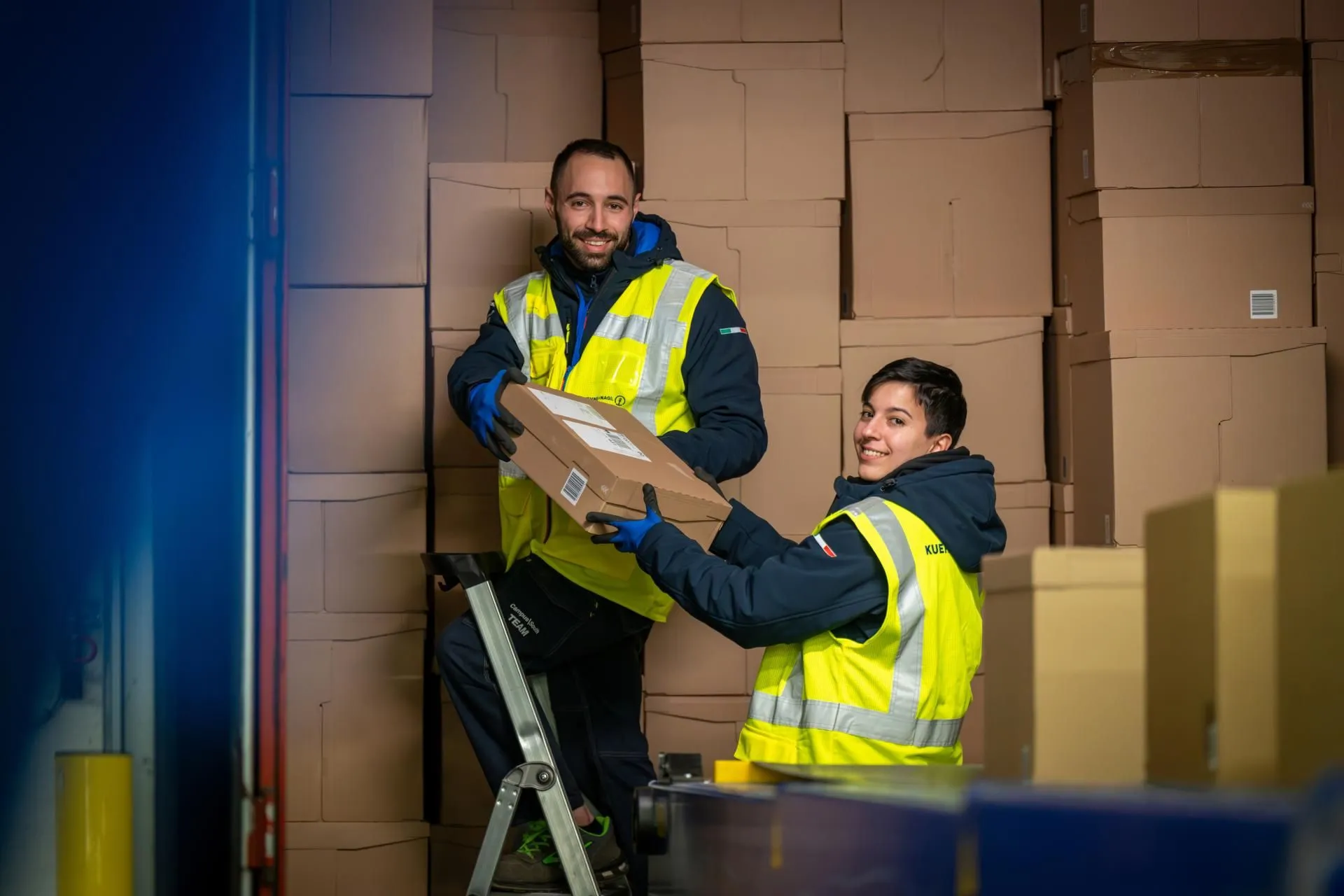 Two coworkers helping one another with stacking boxes in a warehouse
