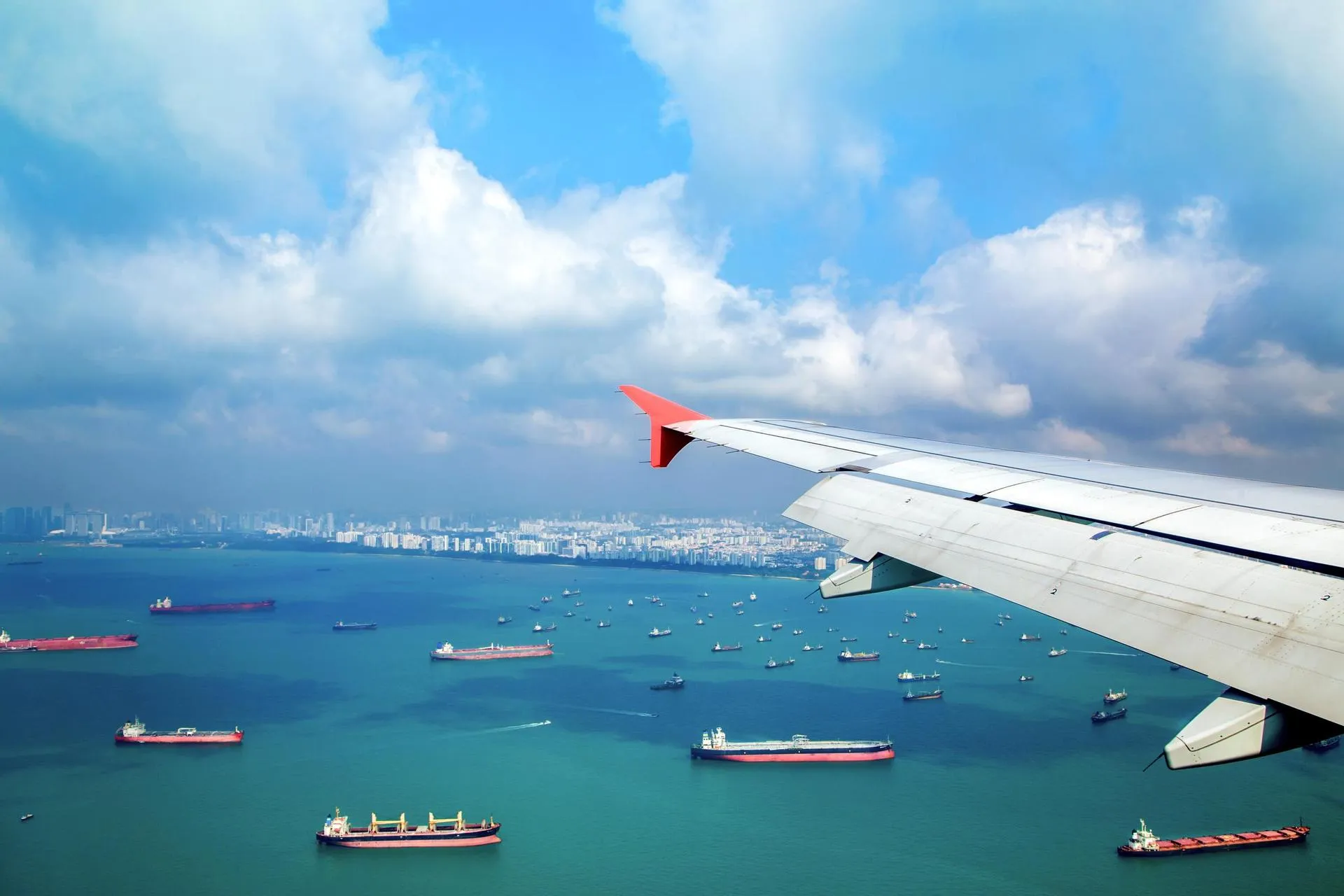 View from a plane over the left wing down to a harbour with container ships.