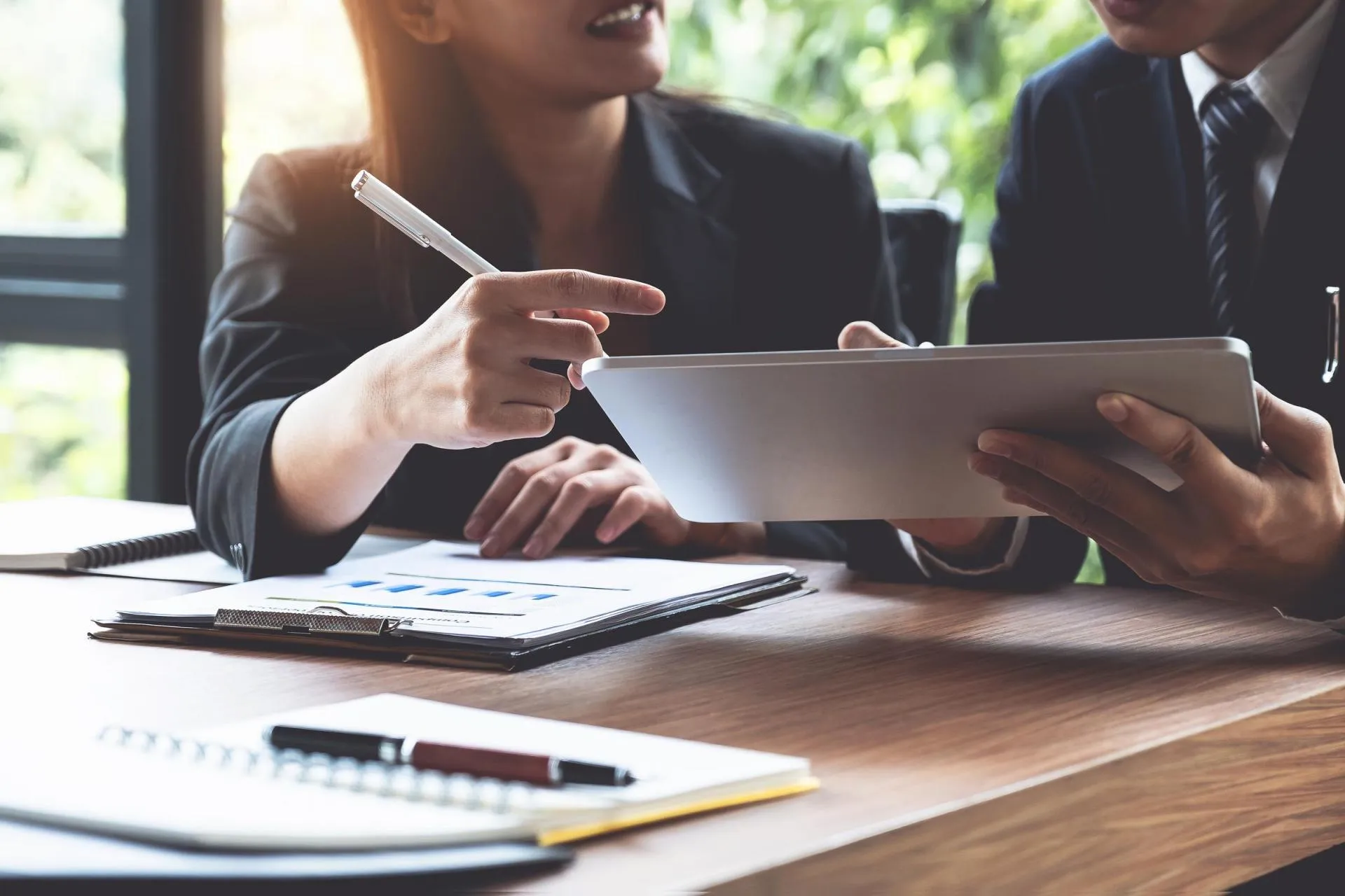 Two business people discussing documents and a tablet at a desk in an office.