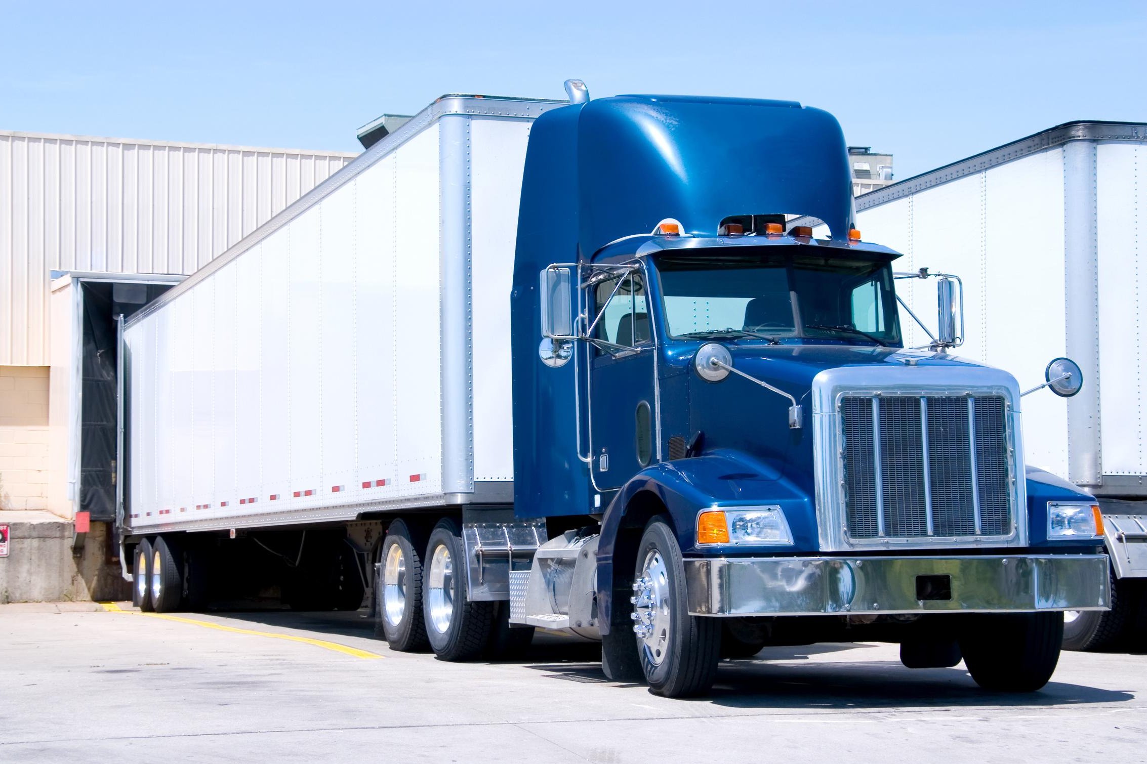 Blue truck with white trailer parked at depot for loading or unloading cargo