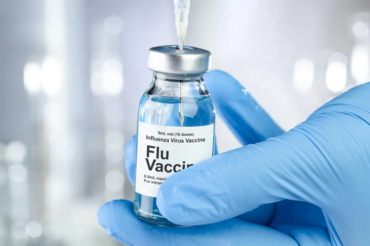 Doctor taking syringe in influenza vaccine bottle with control