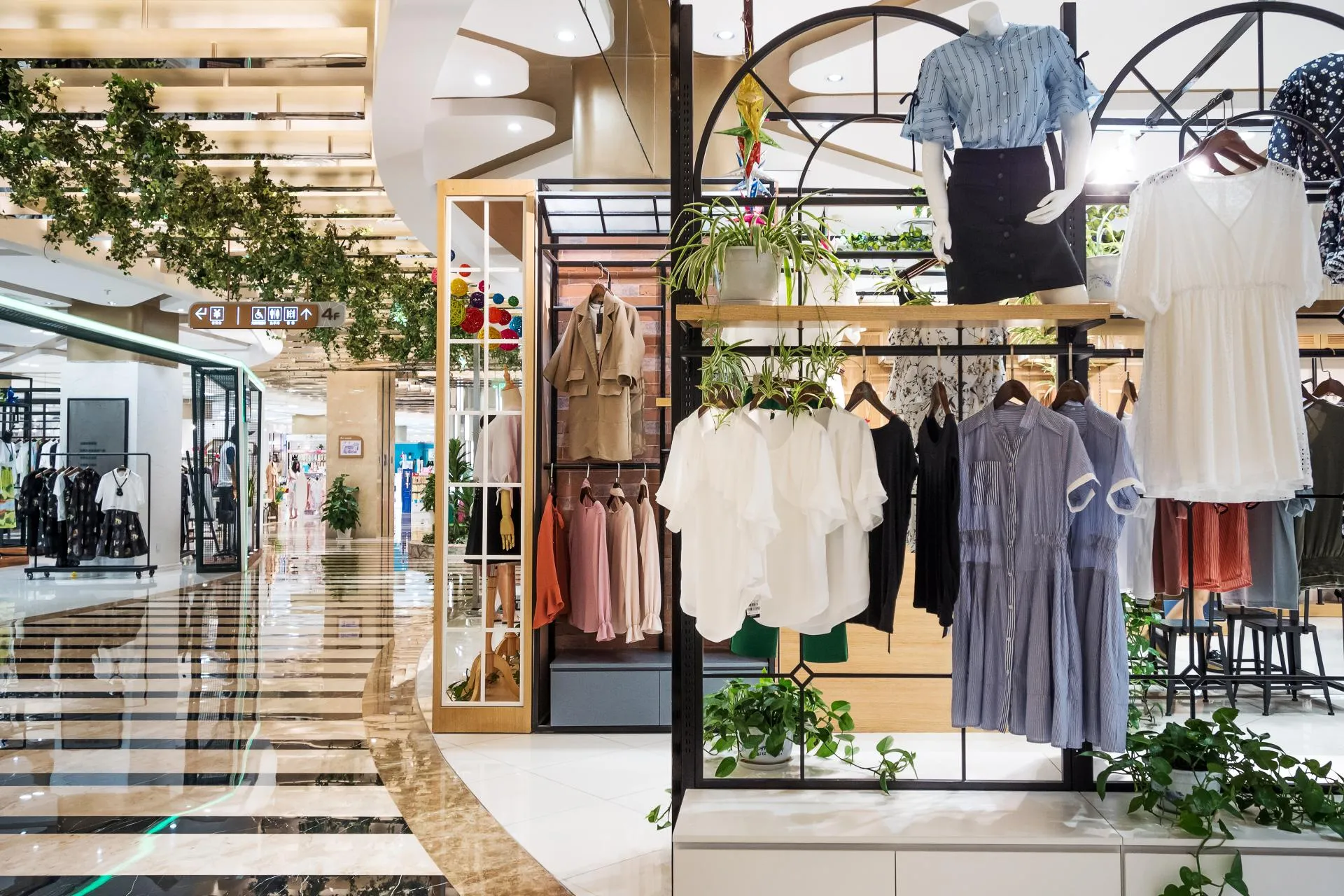 Clothing display inside a modern shopping mall featuring women's apparel on racks and mannequins.