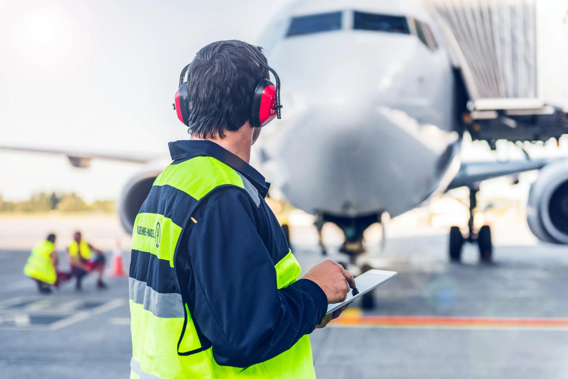 Ground operations worker using a tablet beside a commercial aircraft connected to a boarding bridge at the airport gate.