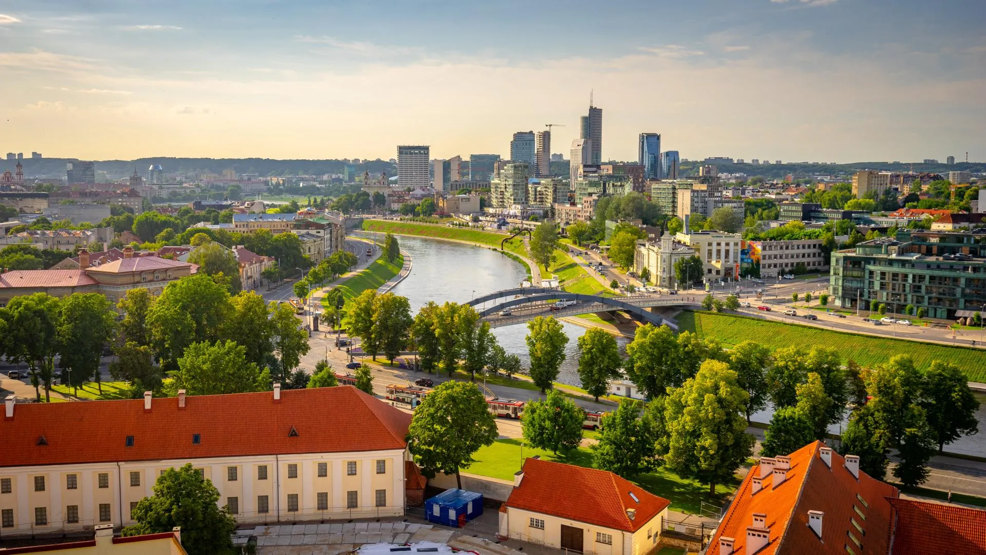 Aerial view of Vilnius, Lithuania, with the Neris River winding through the city, modern high-rise buildings, bridges, and golden autumn trees.