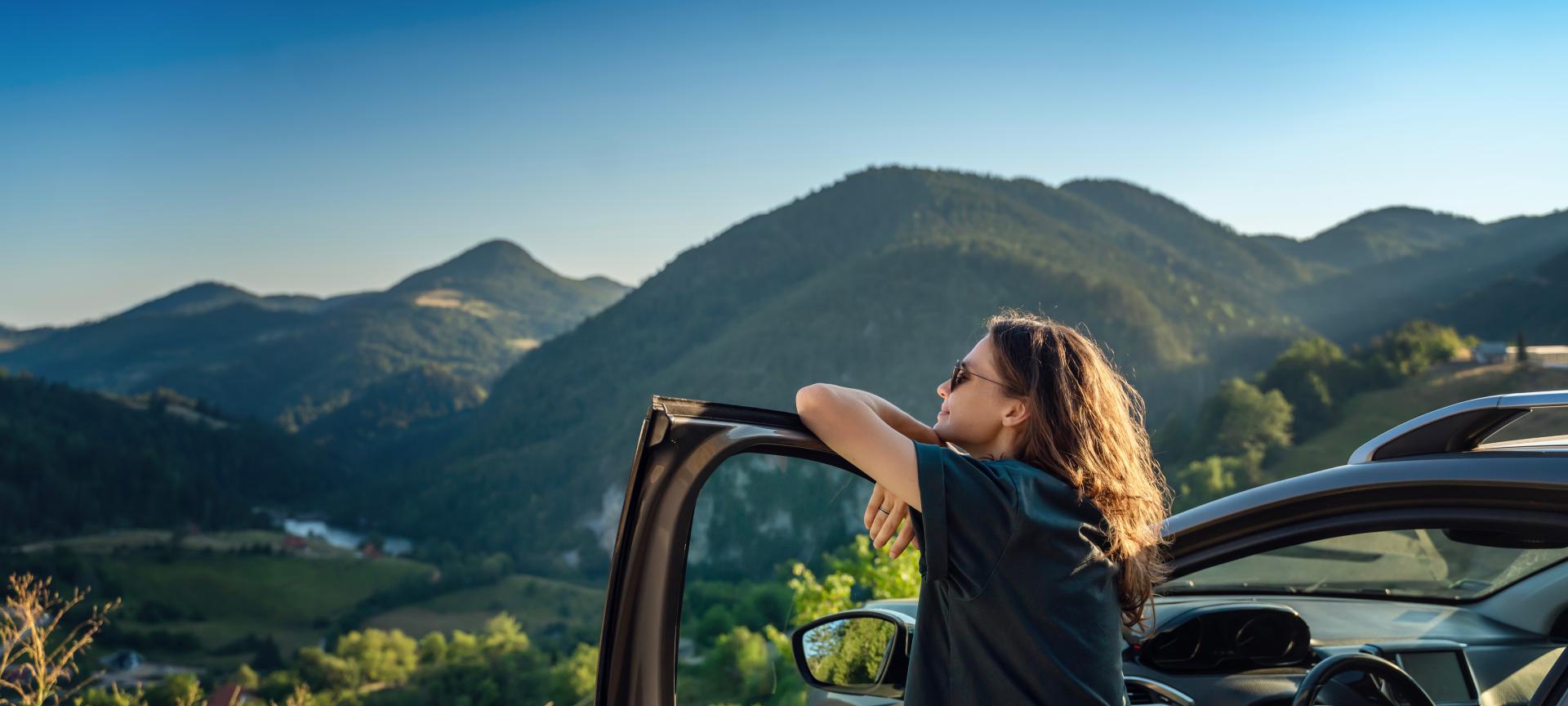 Junge Frau, die mit dem Auto durch die Berge fährt und in die Natur blickt.