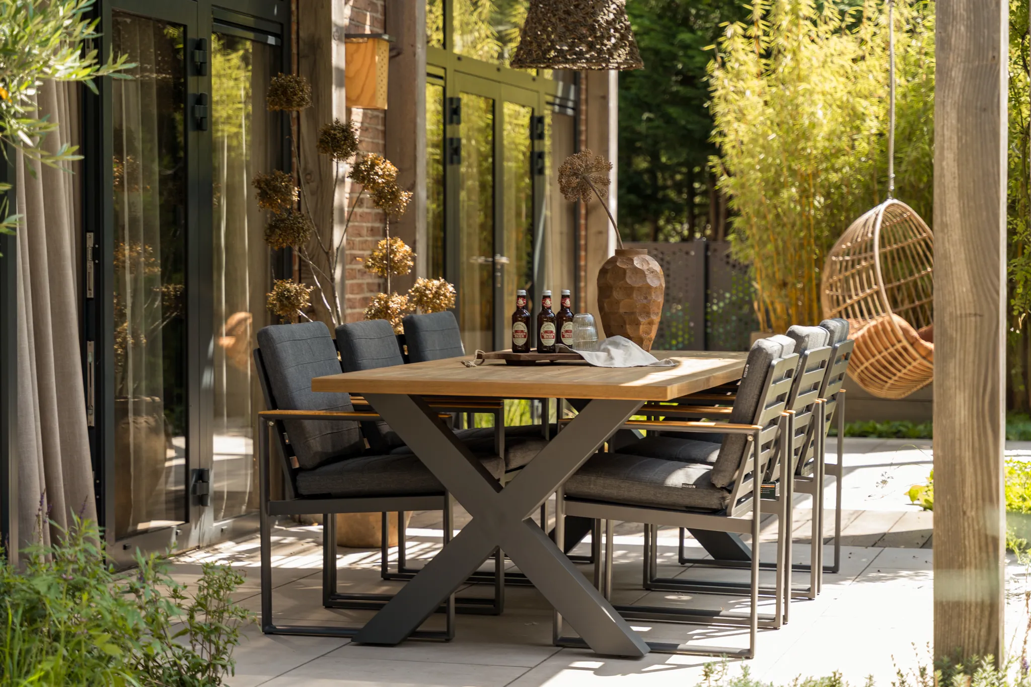 A grey dining table with chairs outside on a terrace in a garden.