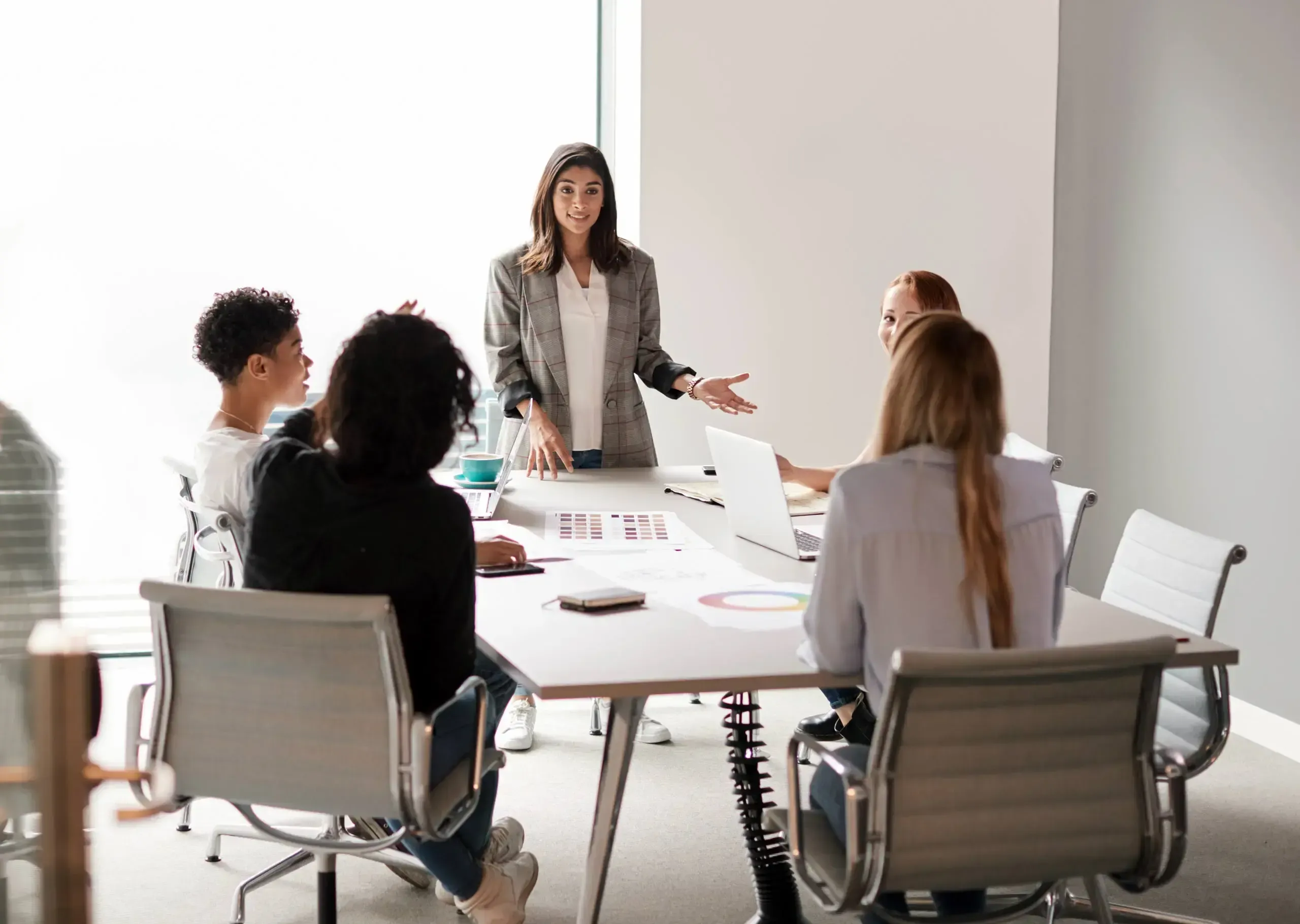 A woman in an office standing in front of an audience around a table