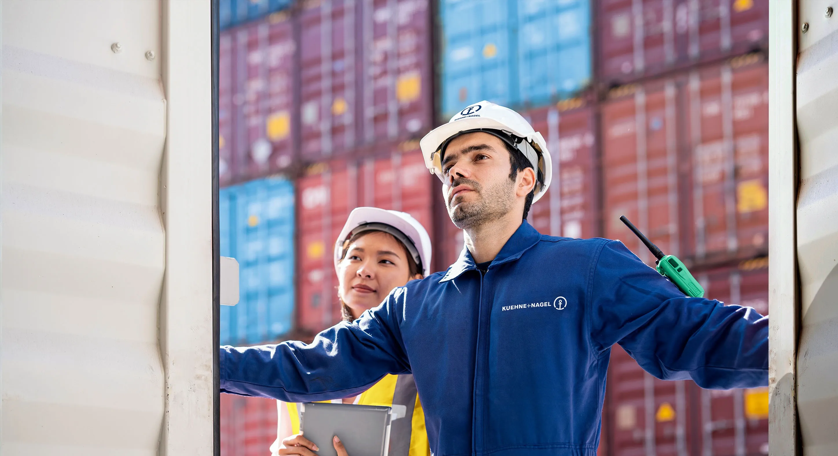 Two Kuehne+Nagel container yard workers are overseeing the transport of a container.