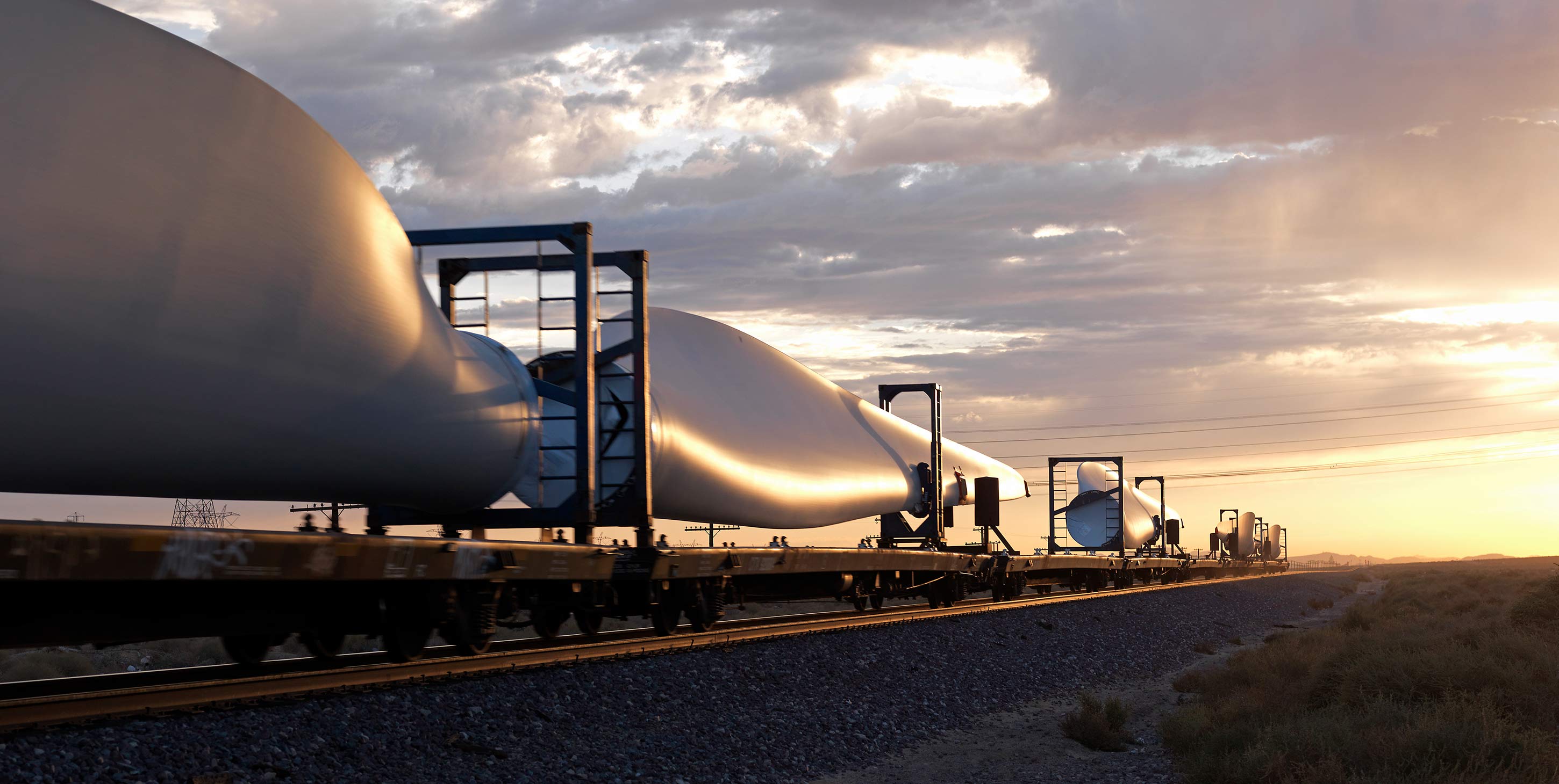 Train carrying wind turbin wings in sunset