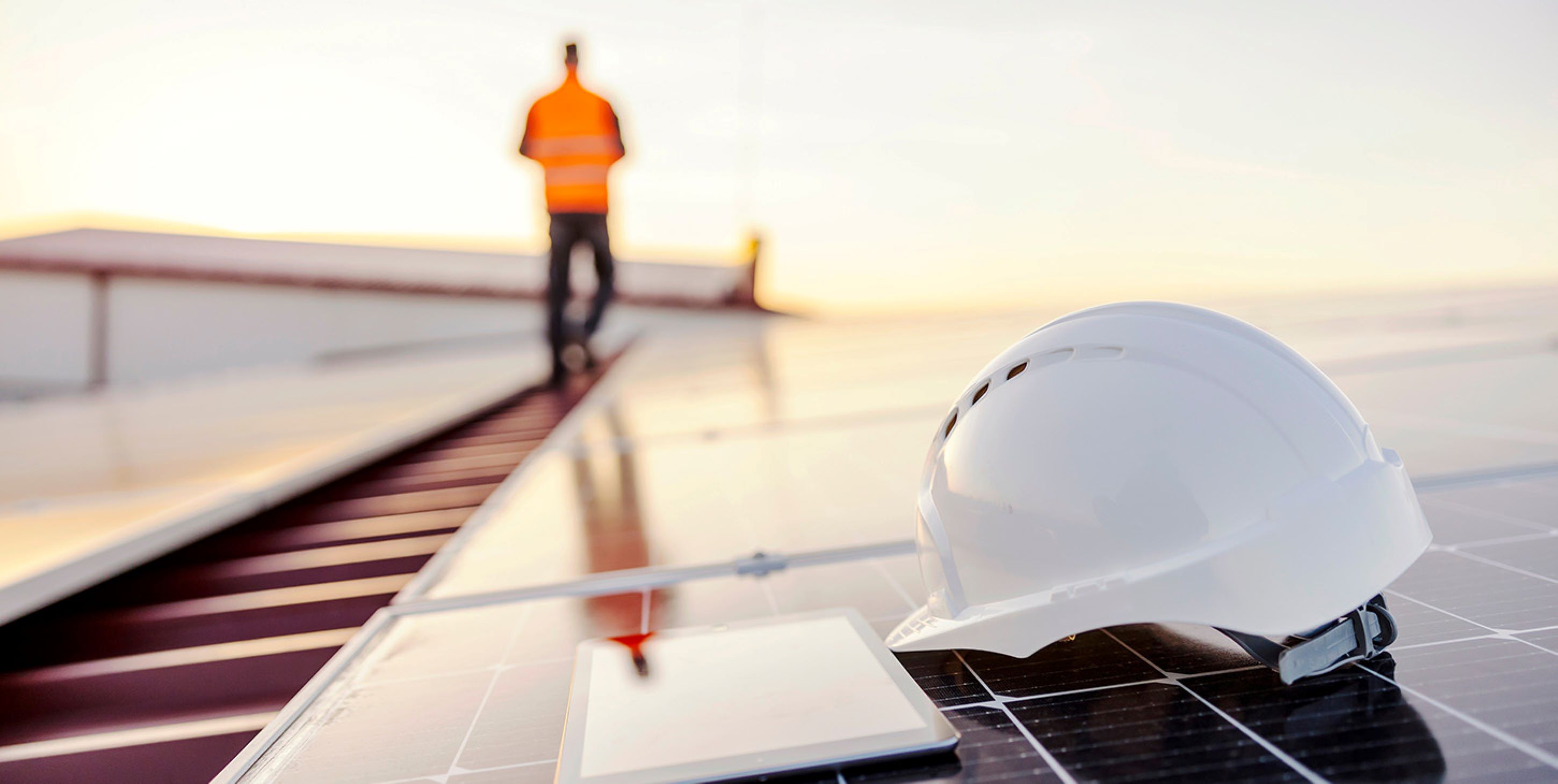Helmet and tablet on solar panels with person in background.