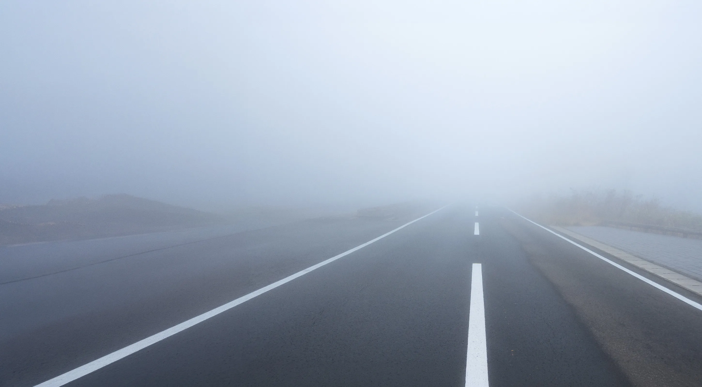 Empty road in dense fog with limited visibility, representing uncertainty, challenges, and the path toward future success.