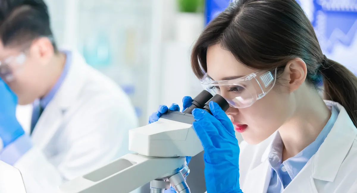 Asian woman looking through a microscope something about healthcare, she wears personal protective equipment