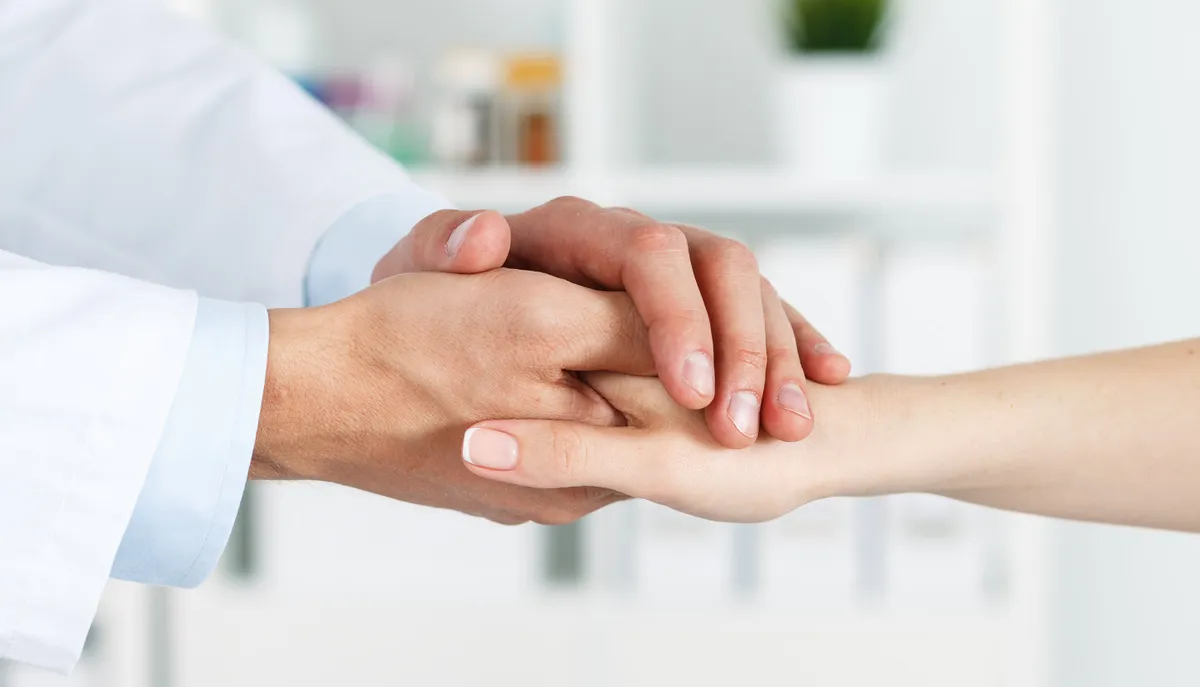 Male doctor (his gown is visible) holding the hand of a female patient