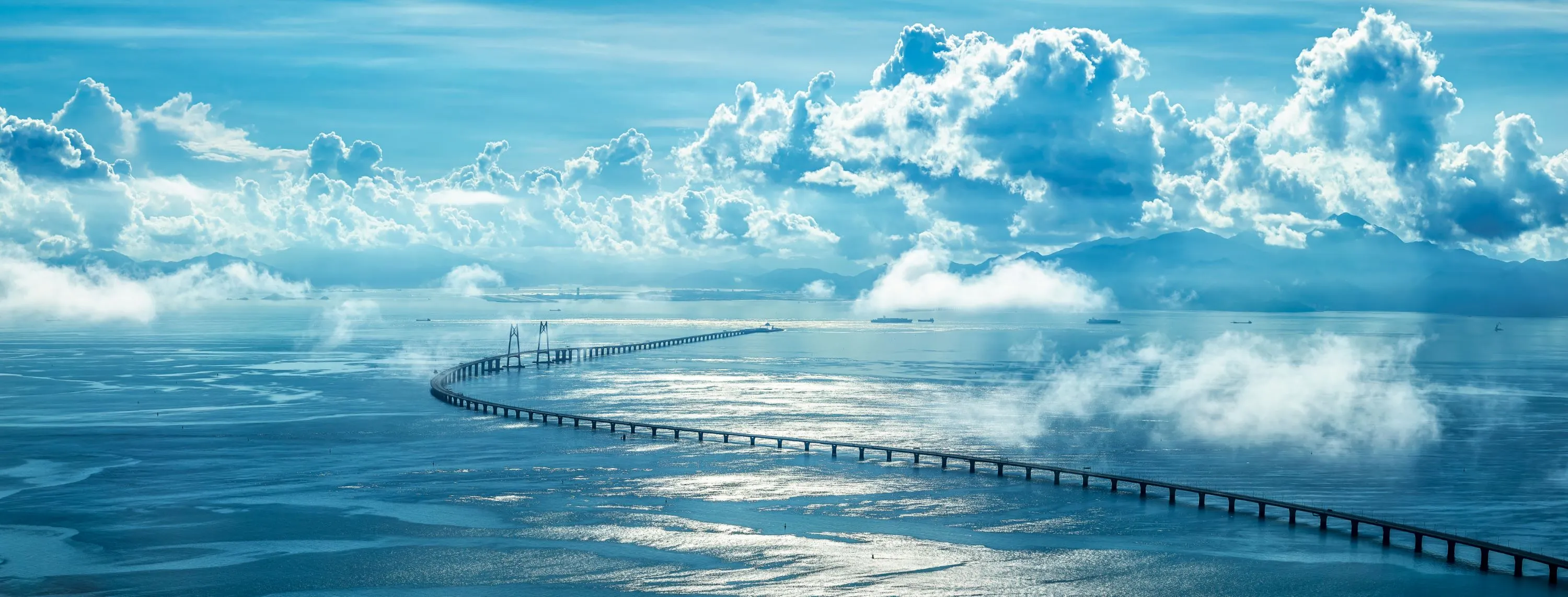 A long bridge leading through sea and clouds towards land