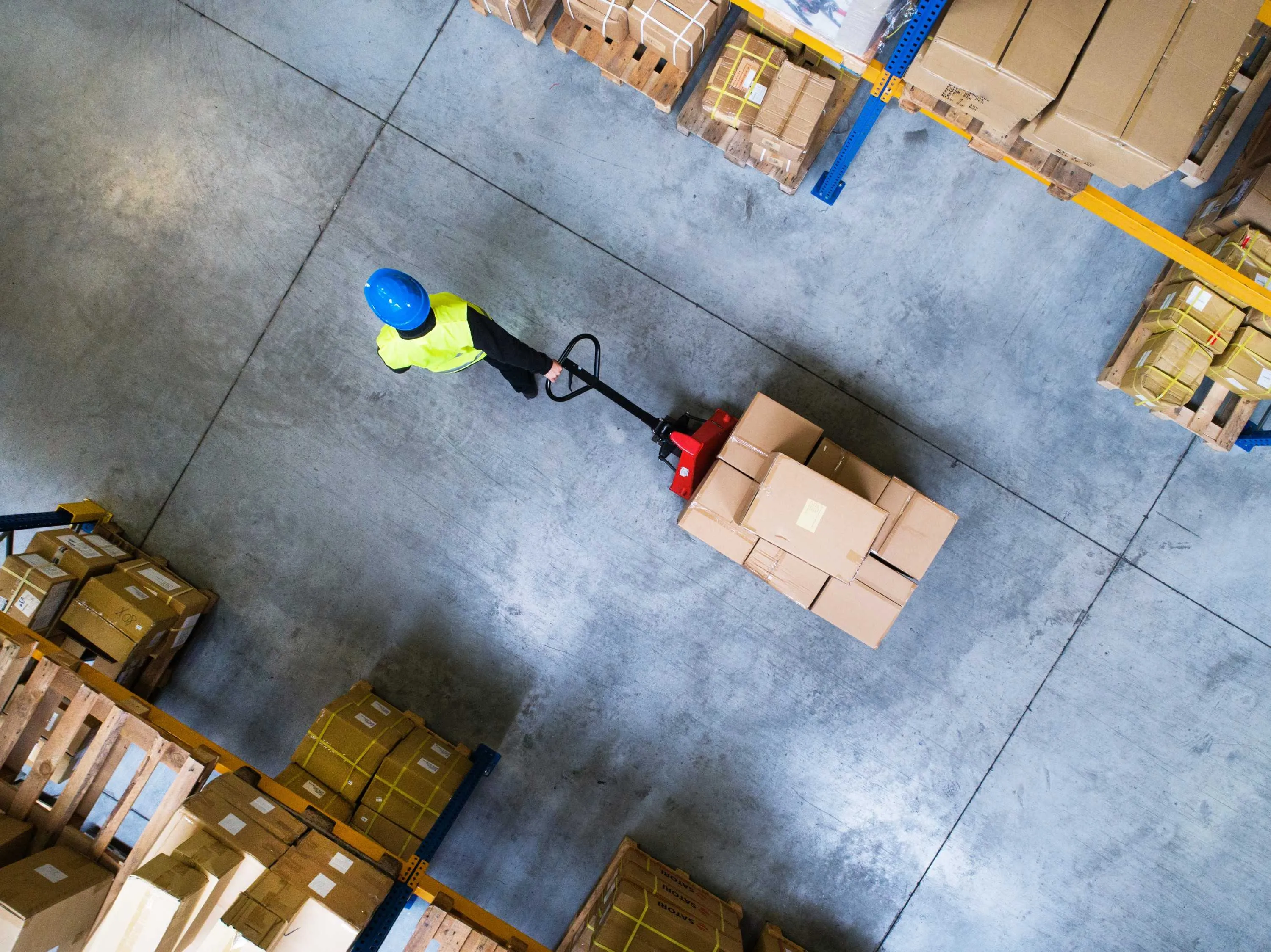 Aerial view of young male warehouse worker pulling a pallet truck with boxes.