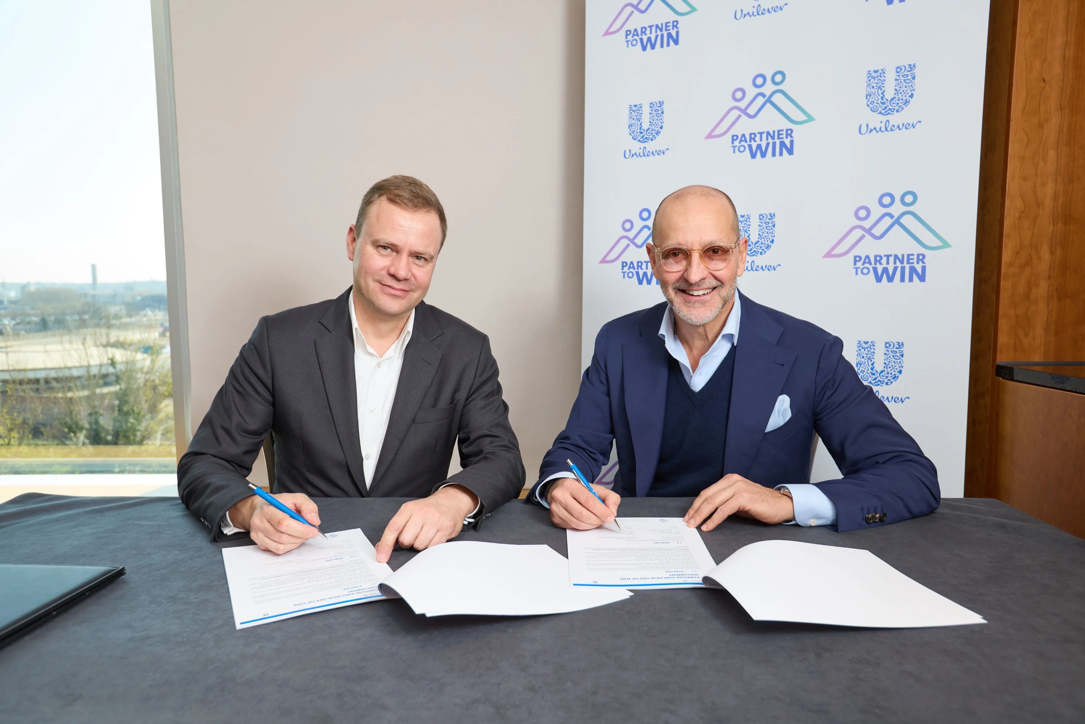 Two businessmen are smiling as they sign documents.