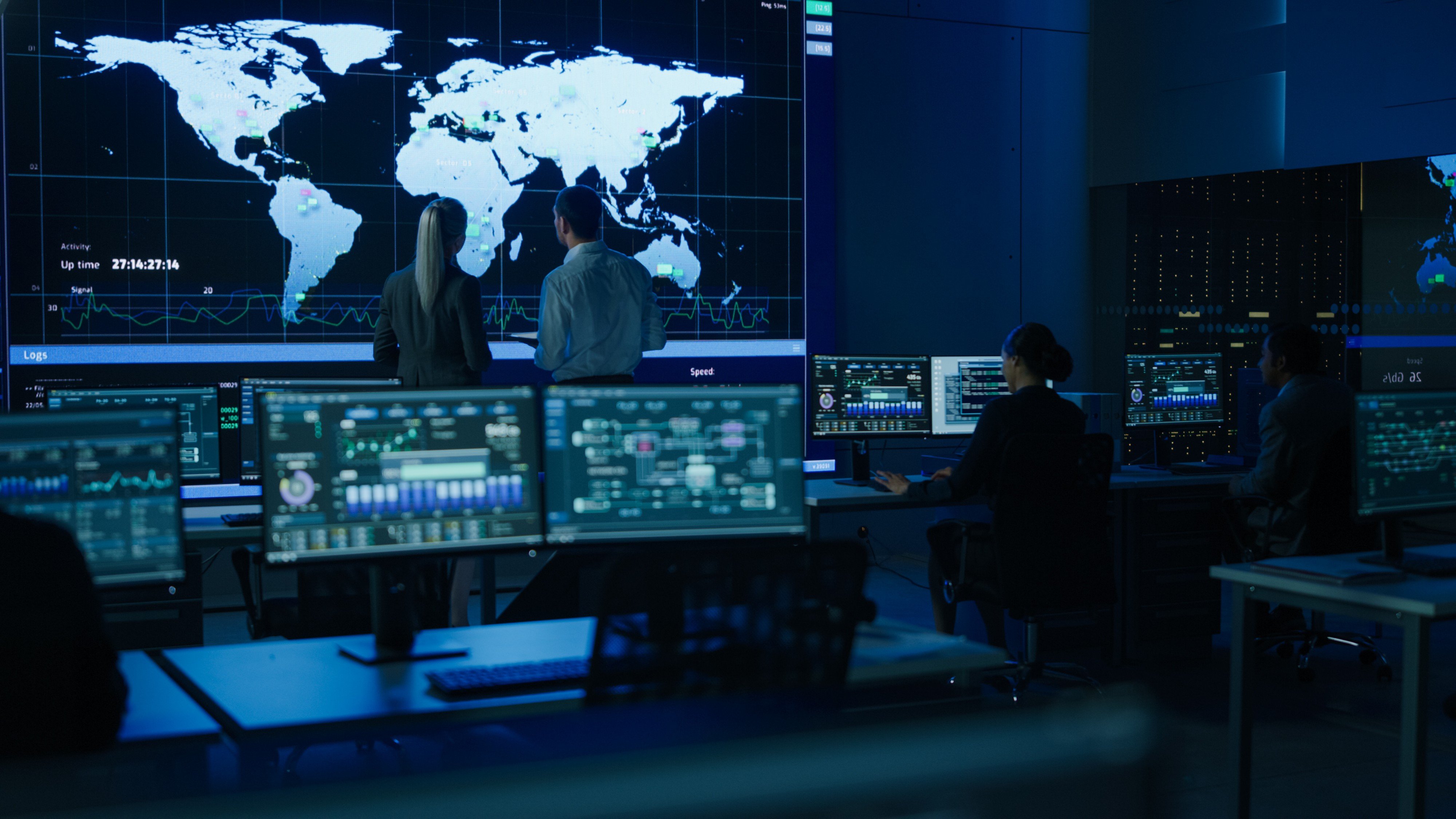 A control room with people monitoring large screens displaying world maps and data.