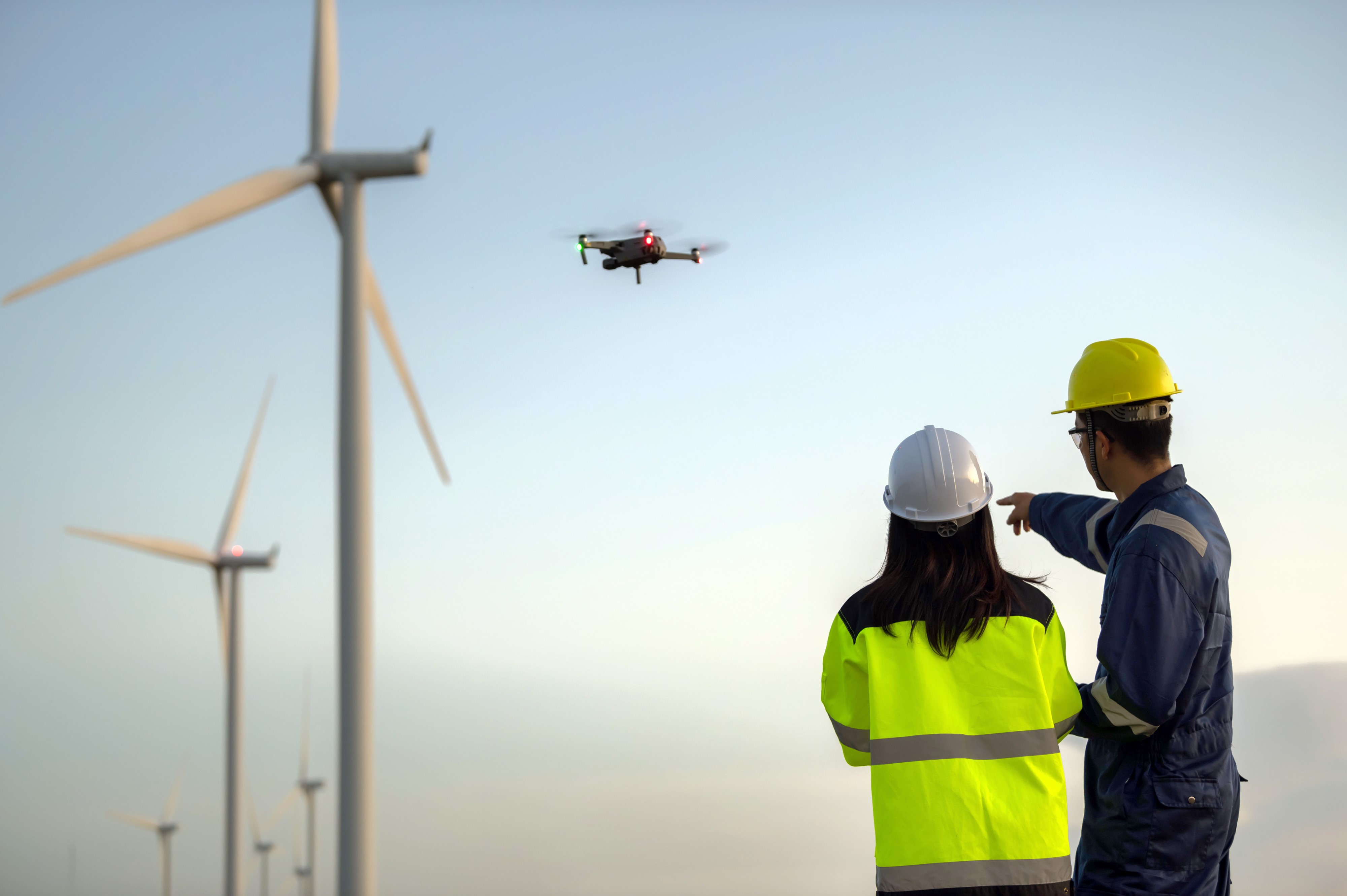 Dois engenheiros trabalhando e segurando o relatório na estação geradora de energia eólica na montanha, Tailândia. Técnico e técnica discutem sobre o trabalho, usando imagens de drone em ângulo elevado.