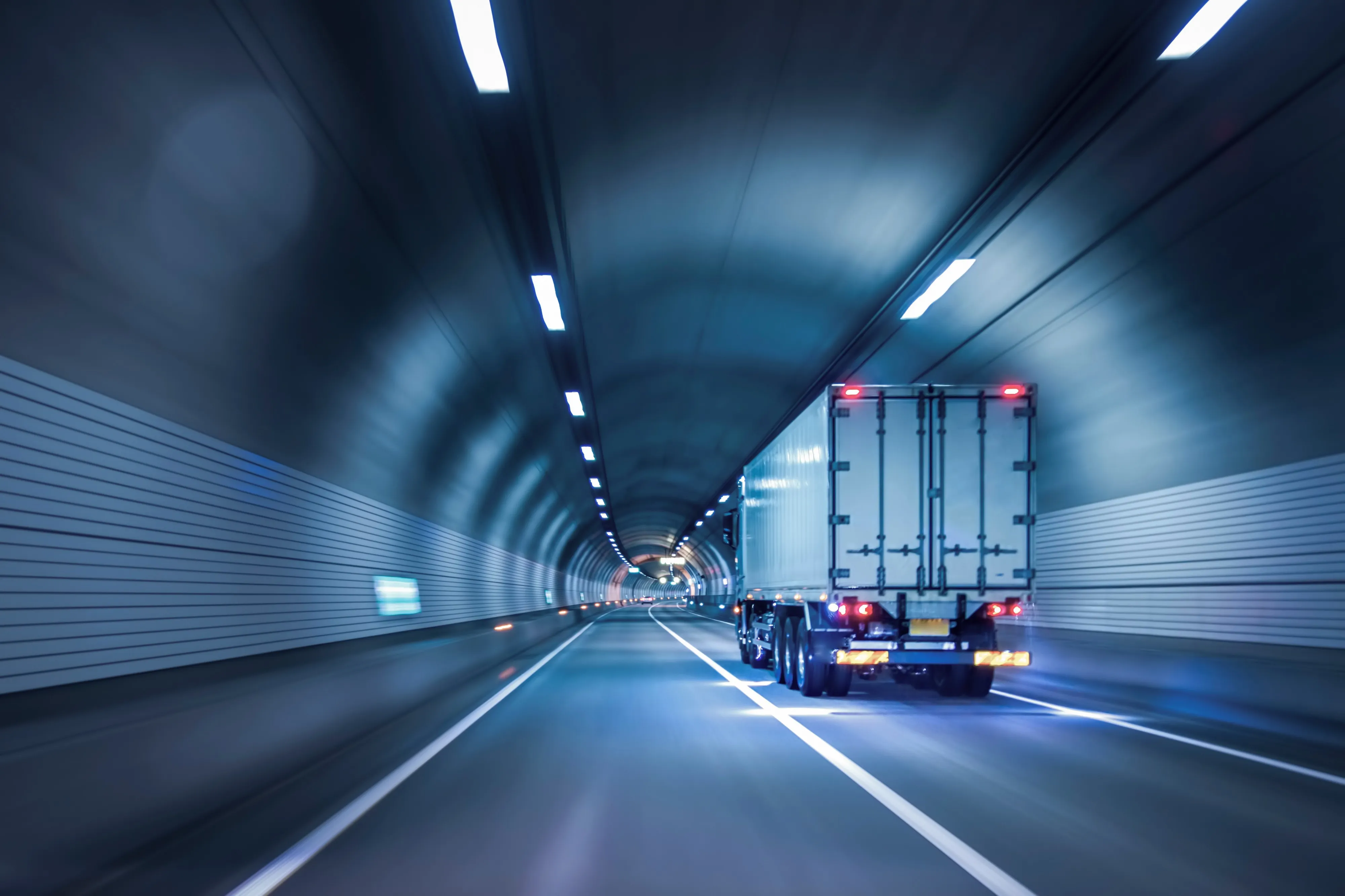 White cargo truck driving through a modern highway tunnel, representing road freight transportation and logistics operations.