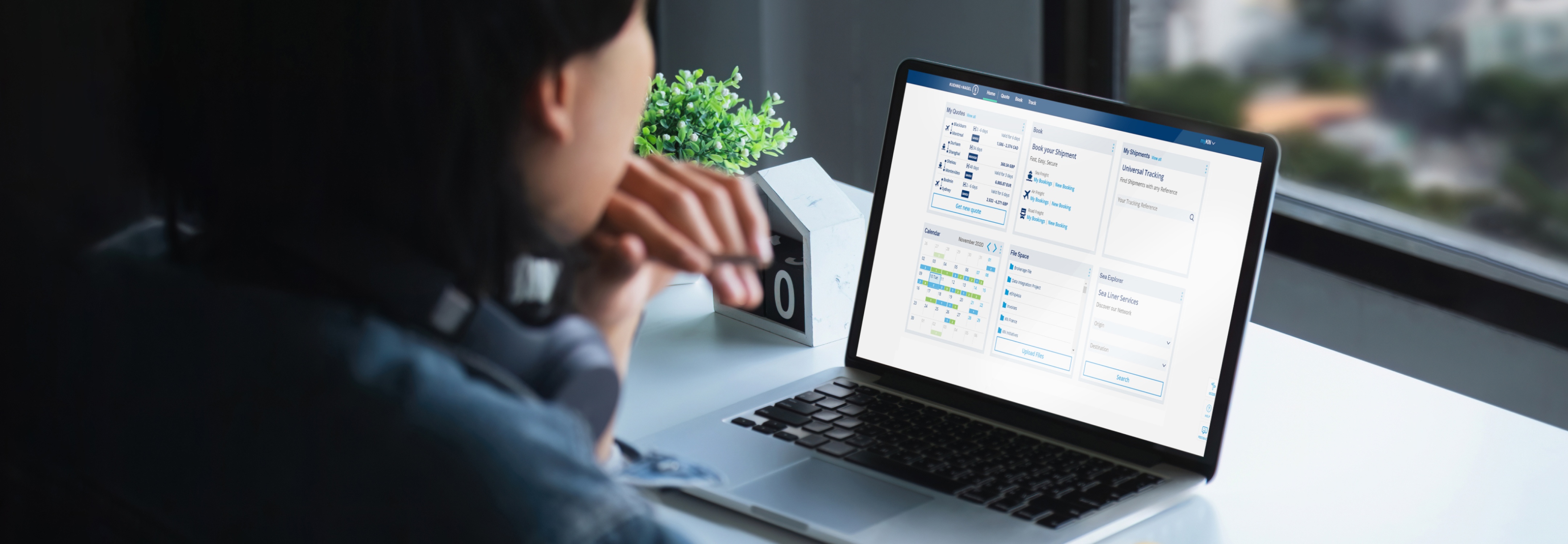 Person procuring freight rate on a laptop displaying a myKN interface, with a plant and desk accessories nearby.