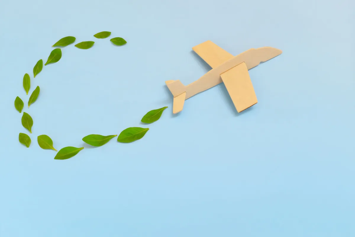 A wooden toy airplane flying and leaving a trail of green leaves against a sky-blue background