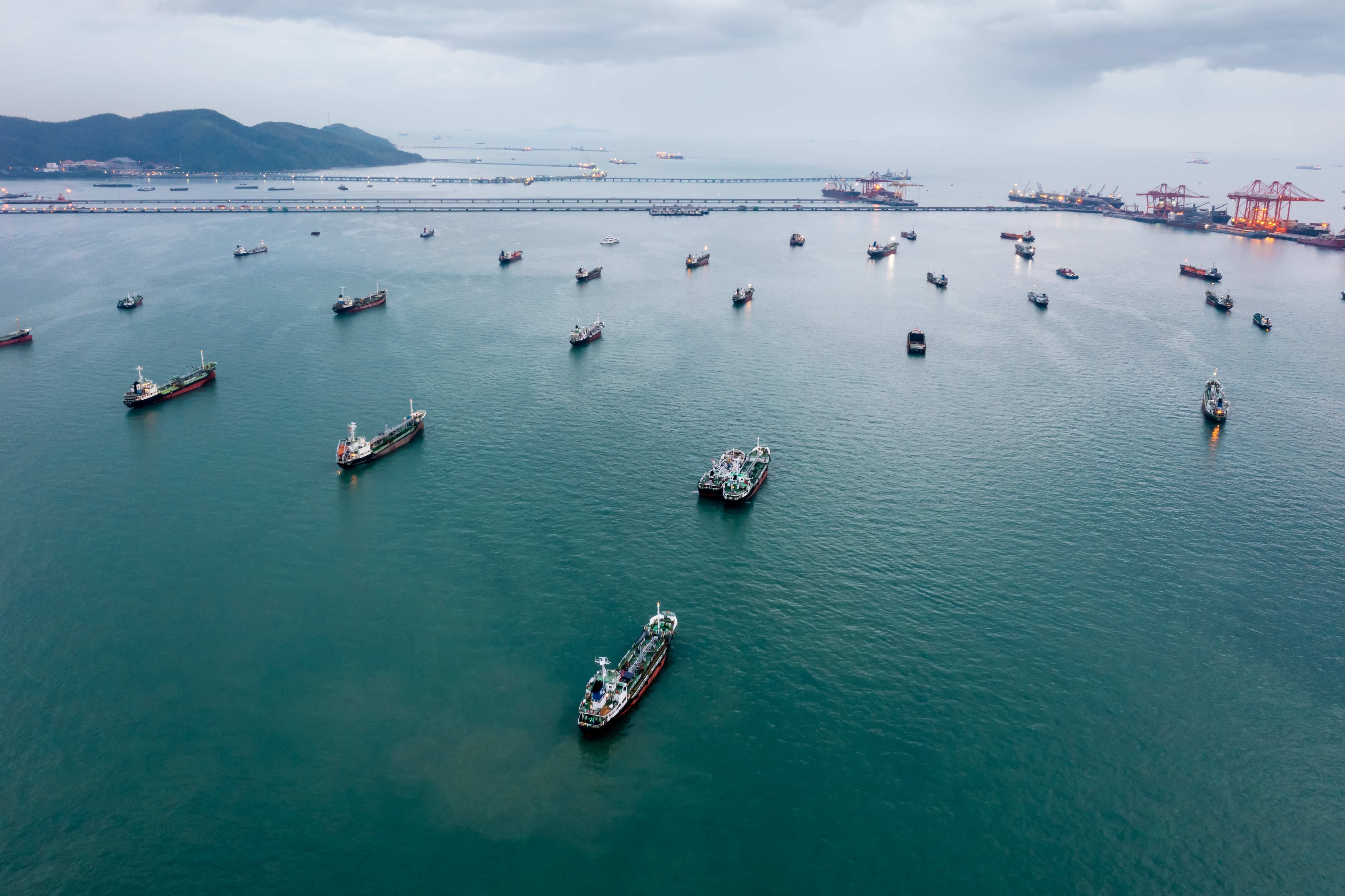 Group of transport ships waiting to carry oil, gas, petrochemicals for export, floating in sea at evening rain storm background aerial view from drone