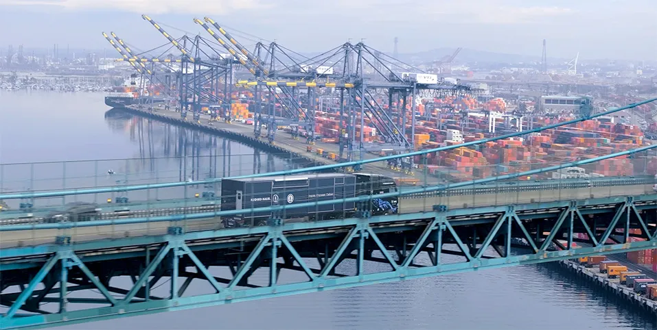 Truck on the road above a bridge that shows a port with sea containers