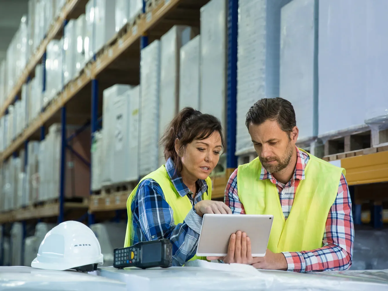 Two employees watching at the tablet in big warehouse