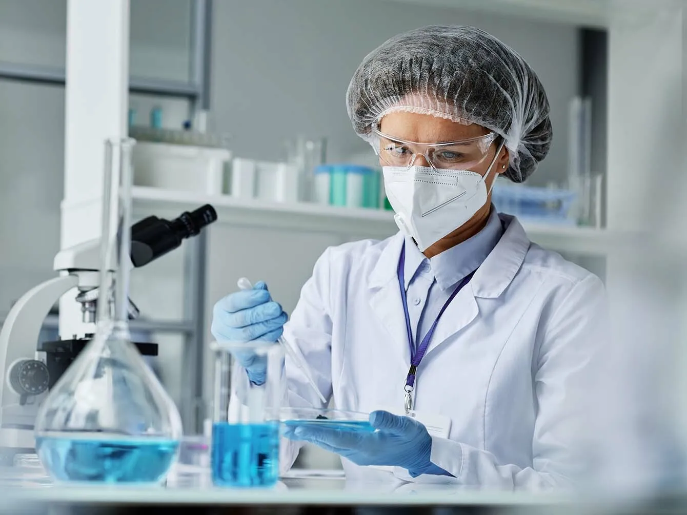 Scientist doing test in a lab, wearing a net on hair and safety glasses and a mask