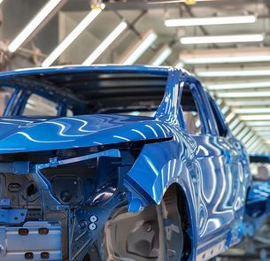 A row of blue car bodies in various stages of assembly is seen on a production line inside a brightly lit automotive factory. The image highlights the precision and scale of modern vehicle manufacturing. A row of blue car bodies in various stages of assembly is seen on a production line inside a brightly lit automotive factory. The image highlights the precision and scale of modern vehicle manufacturing.