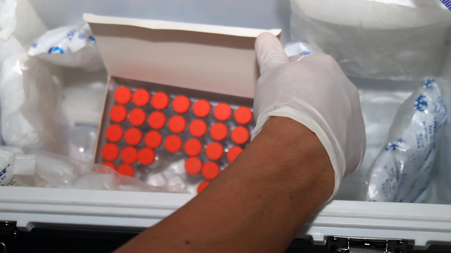 A gloved hand opening a box with red-capped vials