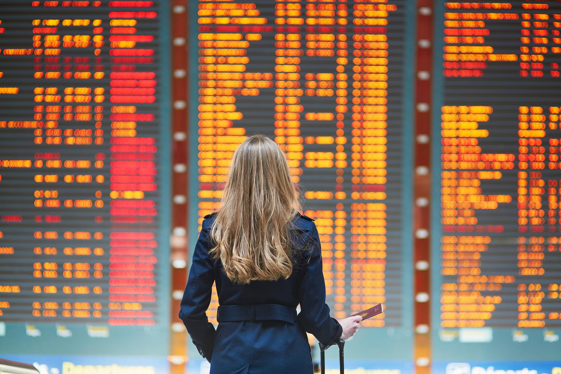 Woman standing in front of a big screen with flight arrivals/departures information