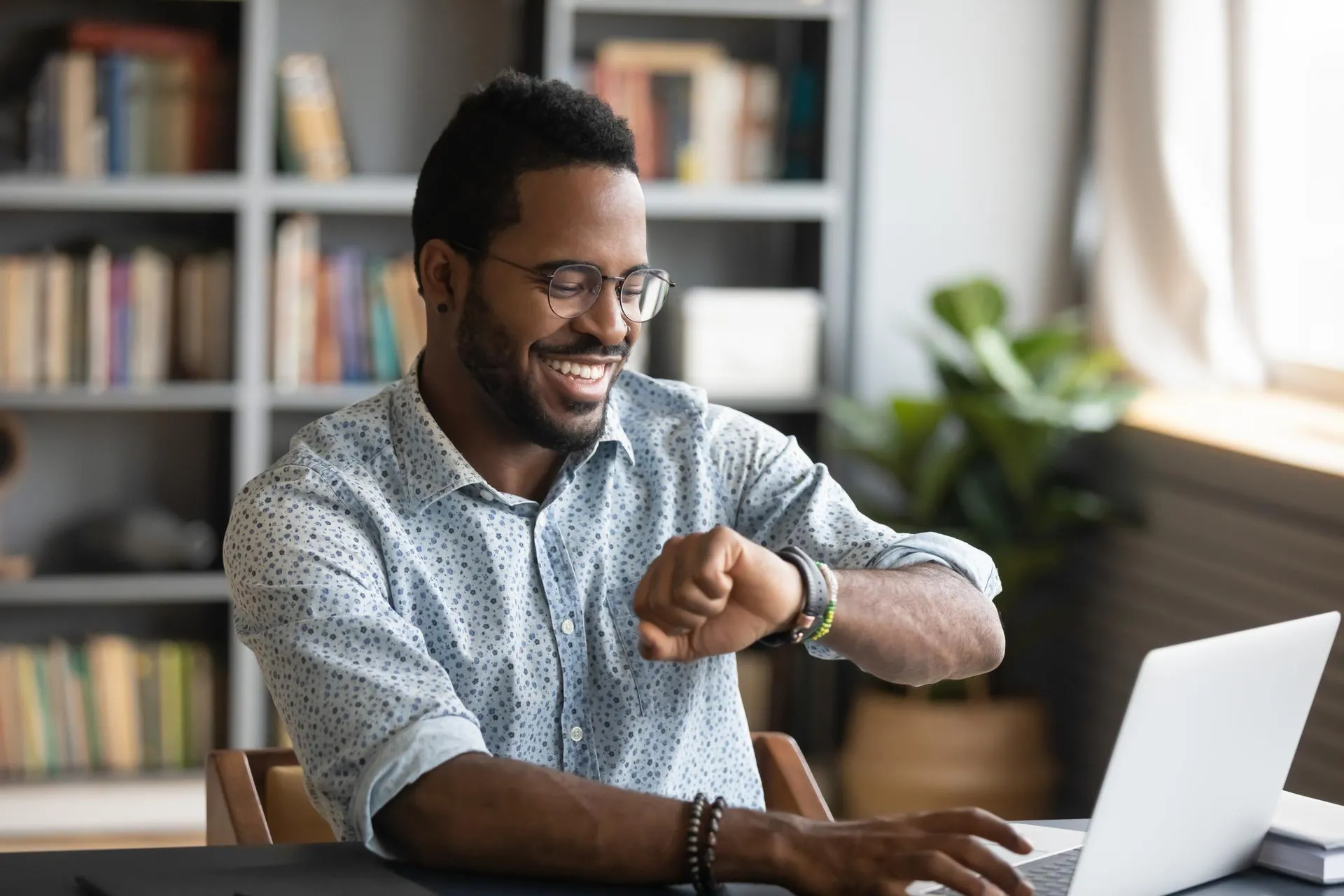 Man smiling, checking the time on his watch, and typing on laptop