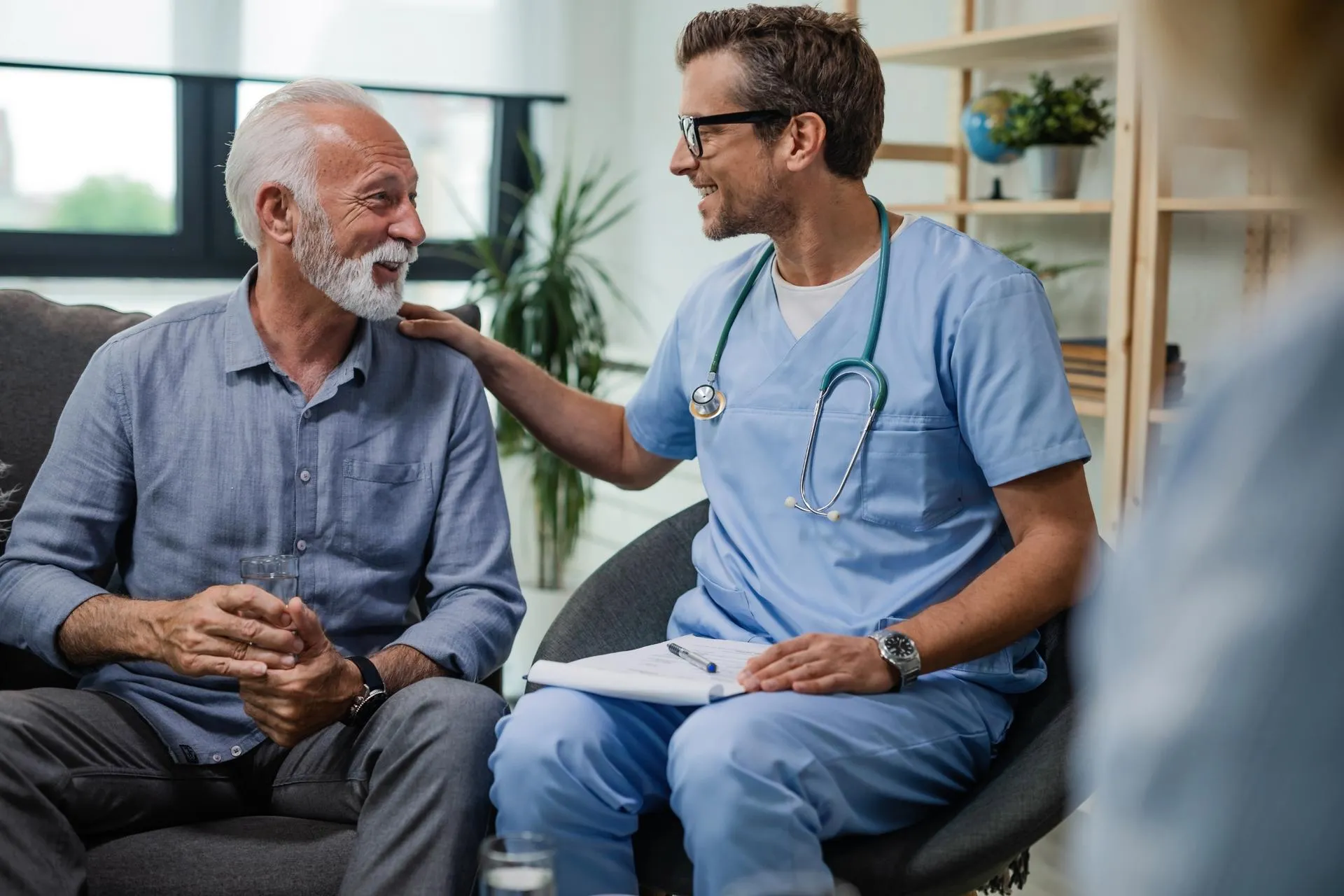 Doctor in home visit with an elderly patient, tapping his shoulder